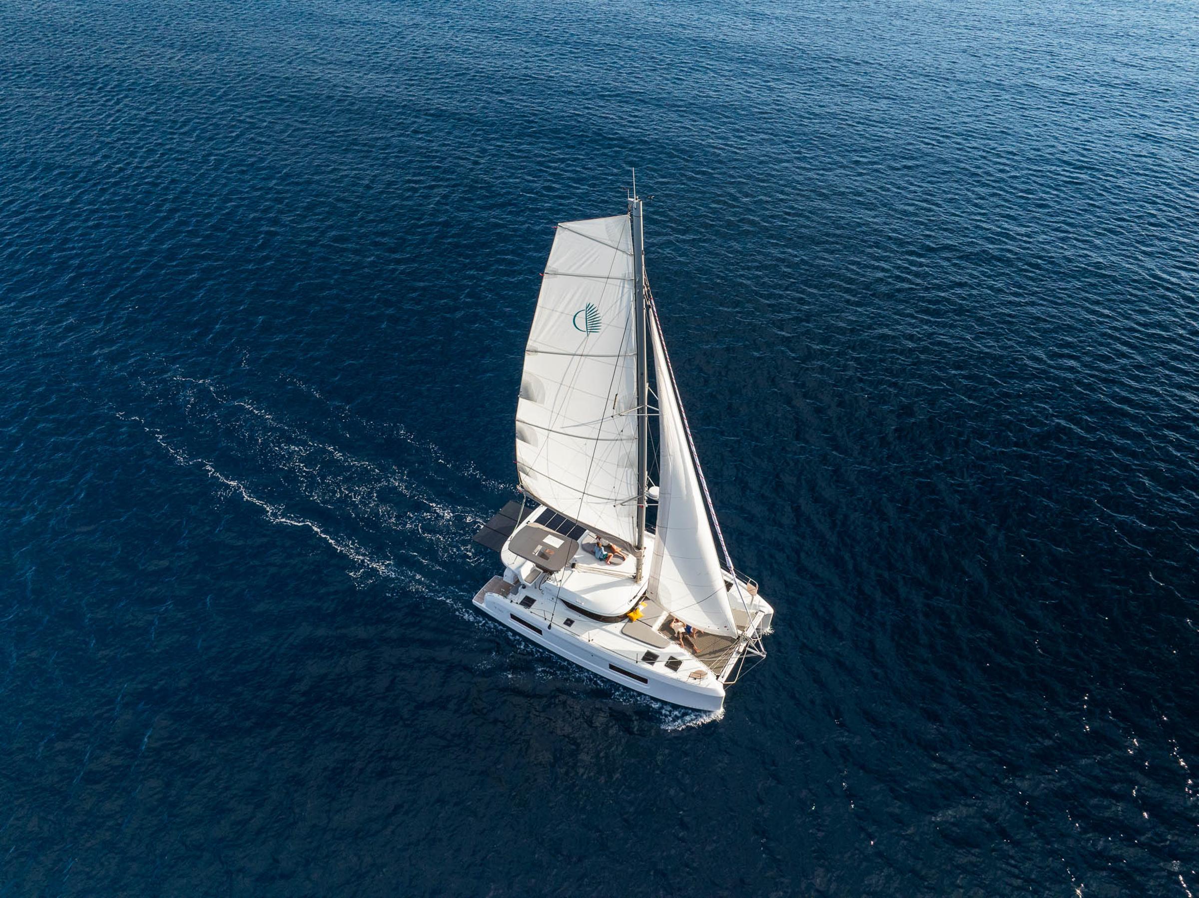 Aerial view of 2025 Lagoon 38 sailing on open blue sea.