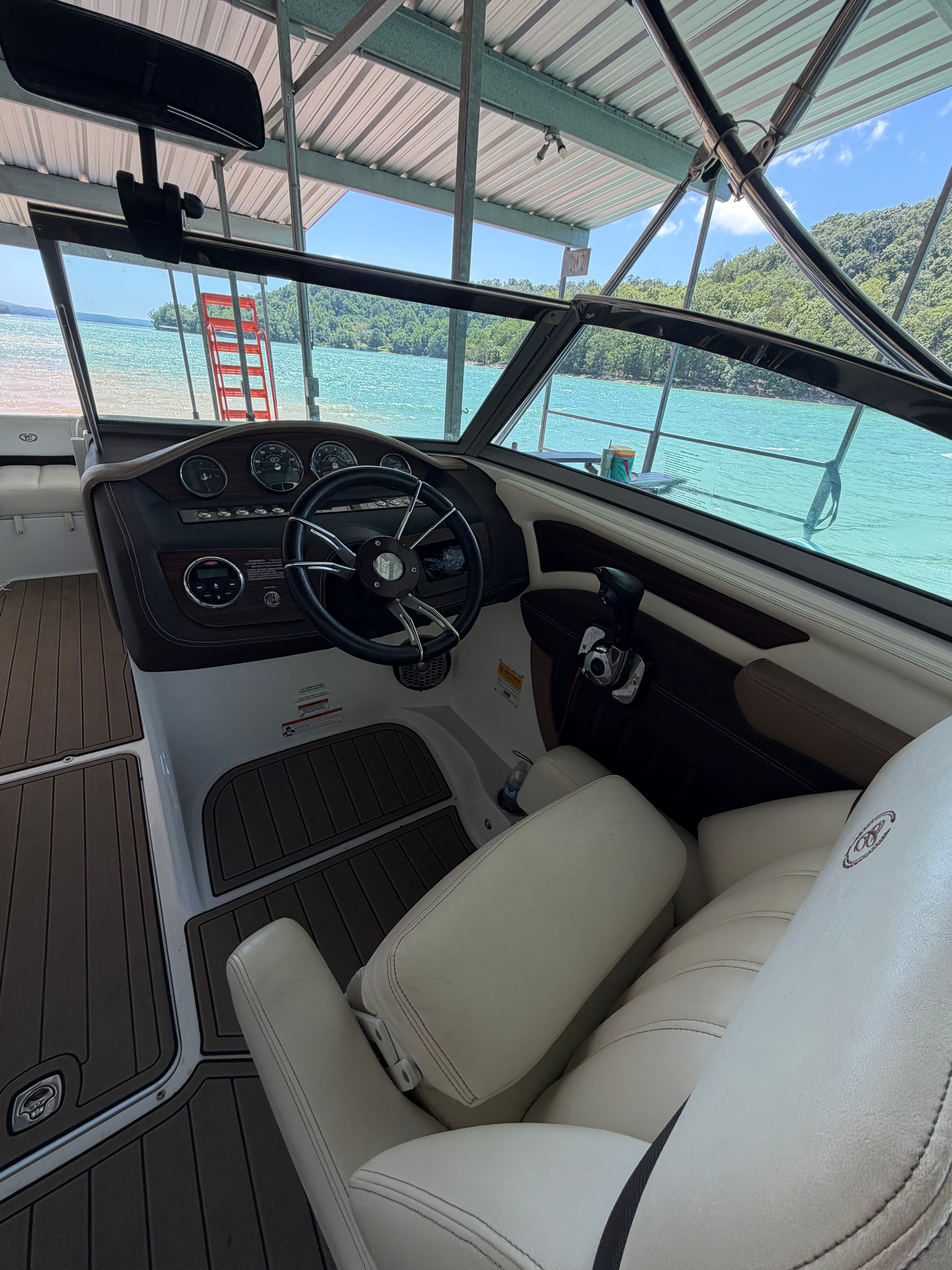 The cockpit of a Cobalt boat with beige seating and steering wheel, docked at a pier.