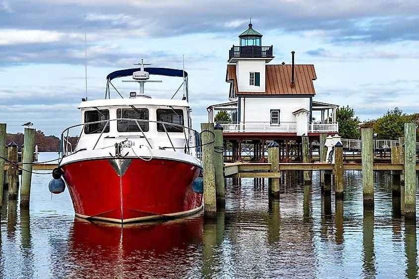 Red 2006 American Tug AT docked near a historic waterfront lighthouse.