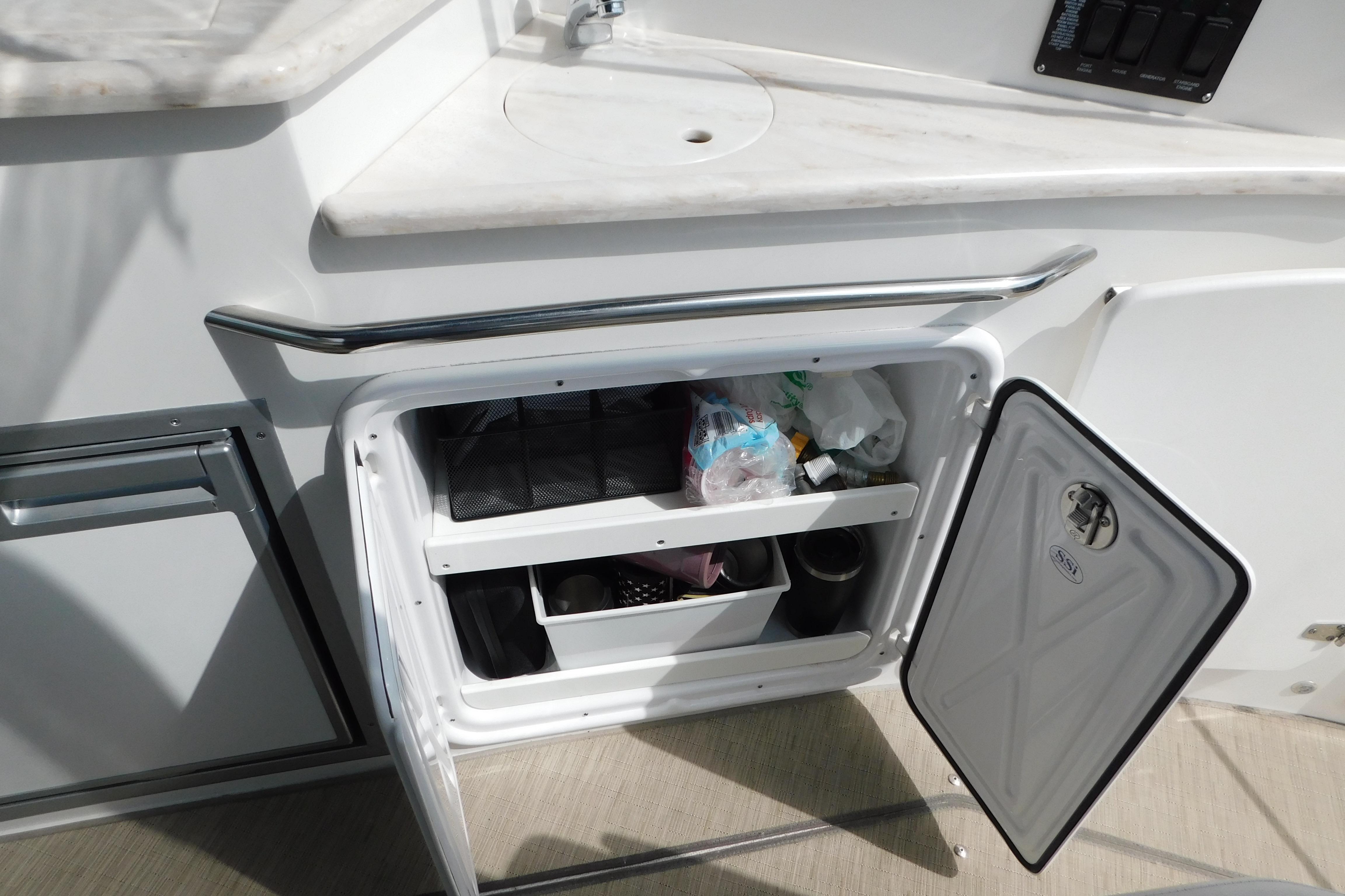 Open storage compartment on 2017 Rinker EX 320 boat with various items inside.