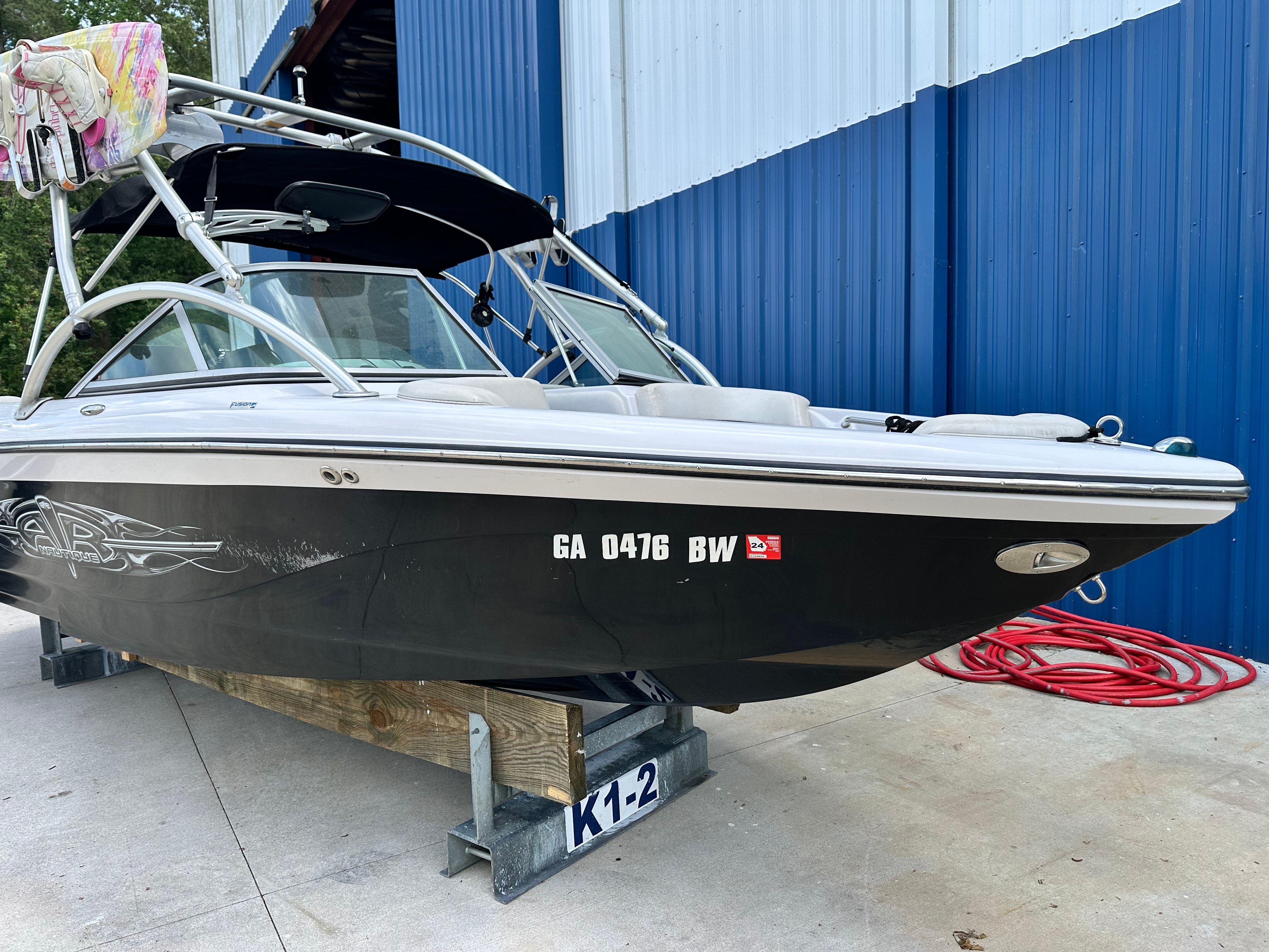 A black 2007 Nautique SV 211 boat is on a block next to a blue building.