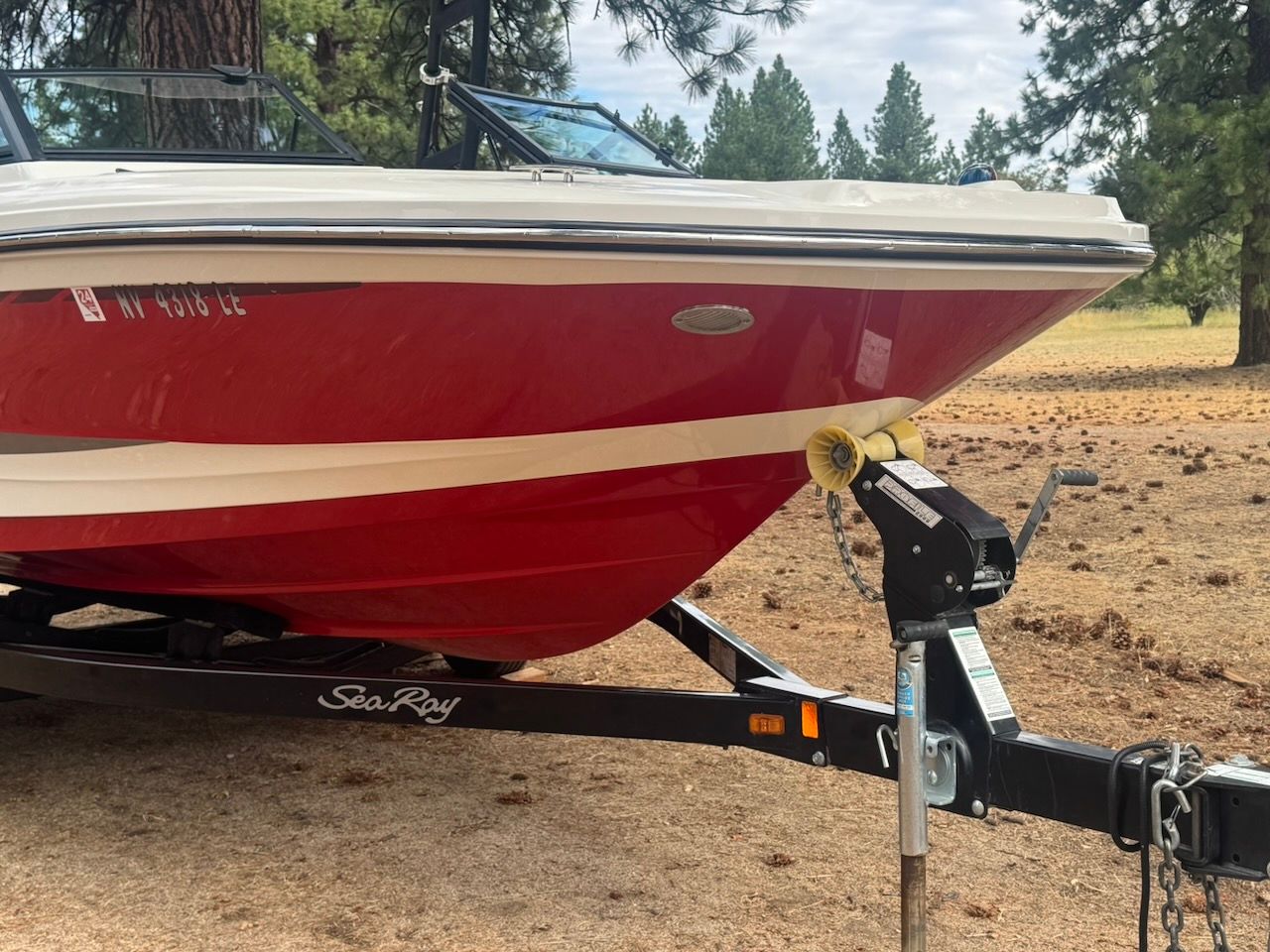 A red 2016 Sea Ray SPX 190 Outboard boat on a trailer in a wooded area.