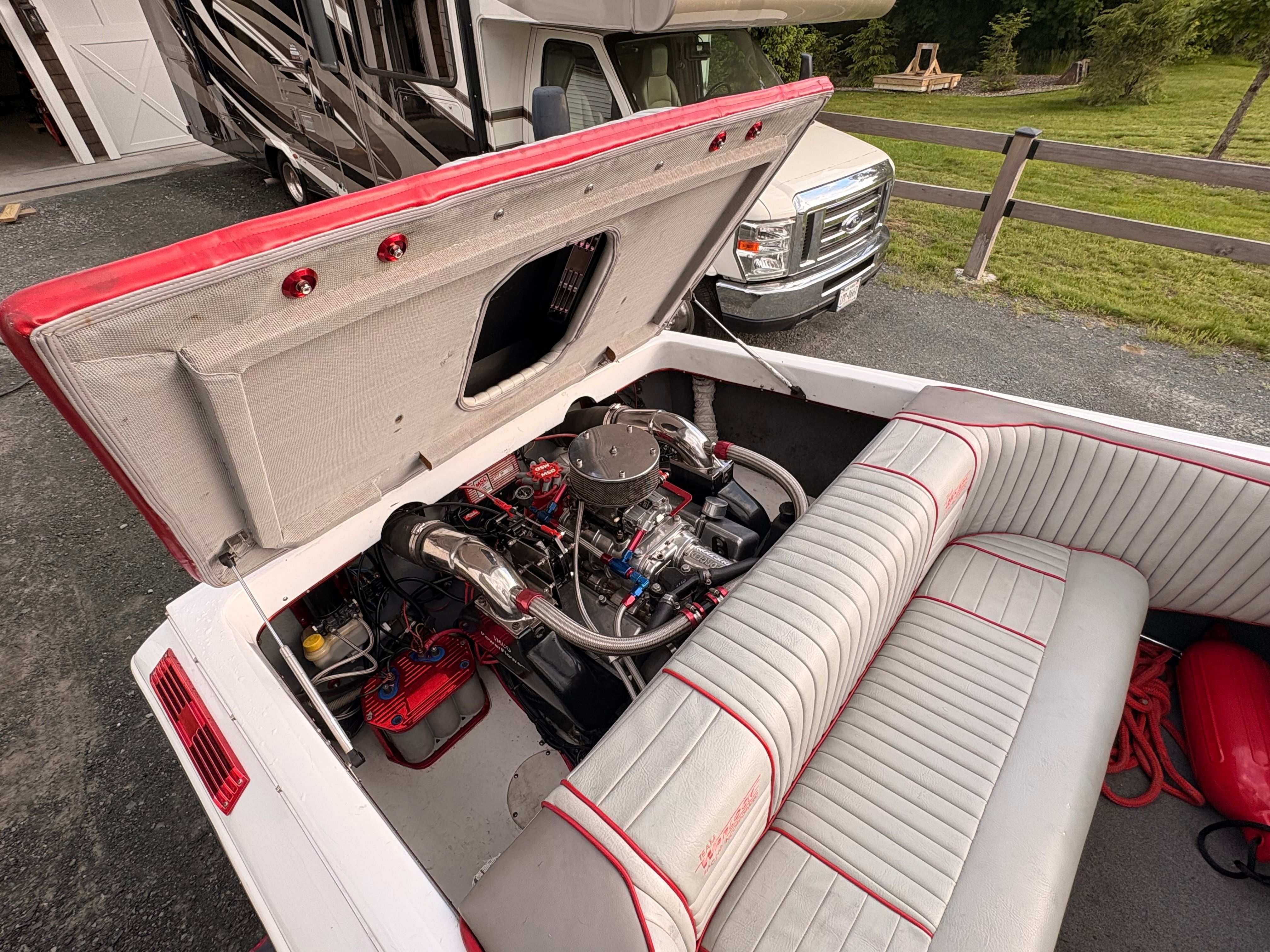 A 1986 Warlock 23 boat with an open engine compartment. The engine is visible, surrounded by white and red upholstery.