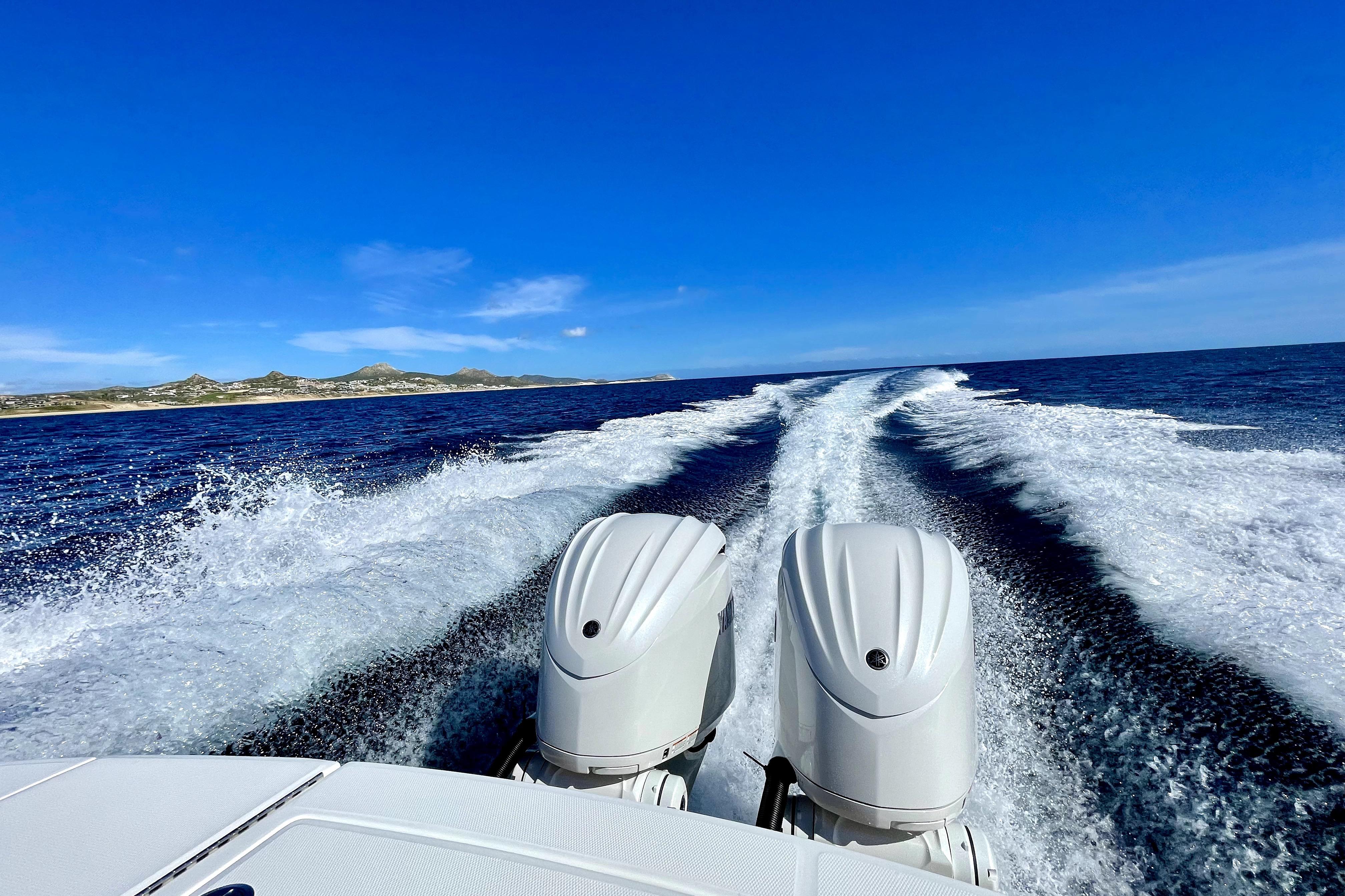 Regulator 28 boat cruising on open sea, leaving a wake behind, under clear blue sky.