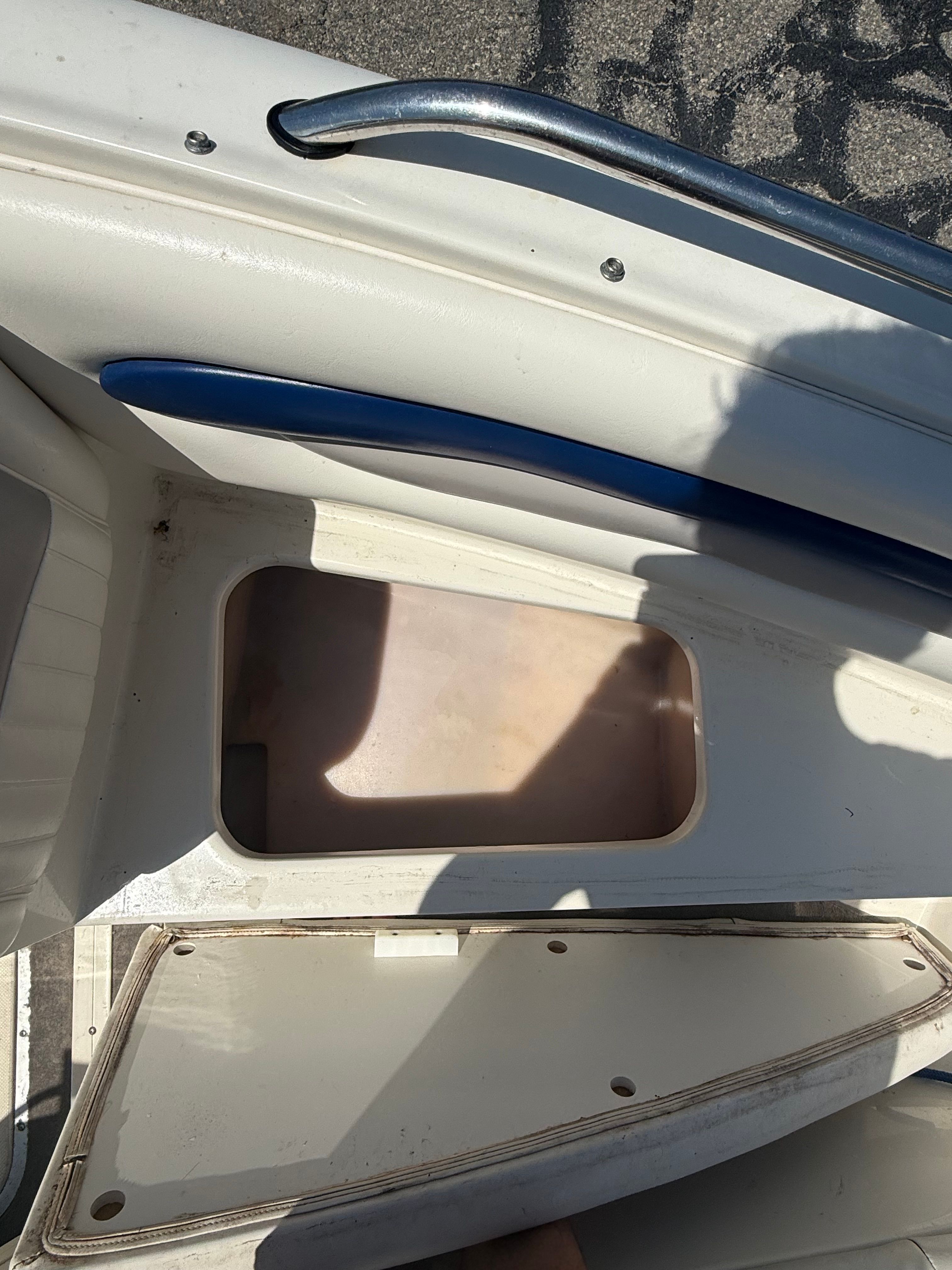 An open storage compartment on a boat with blue upholstery and metal railing.