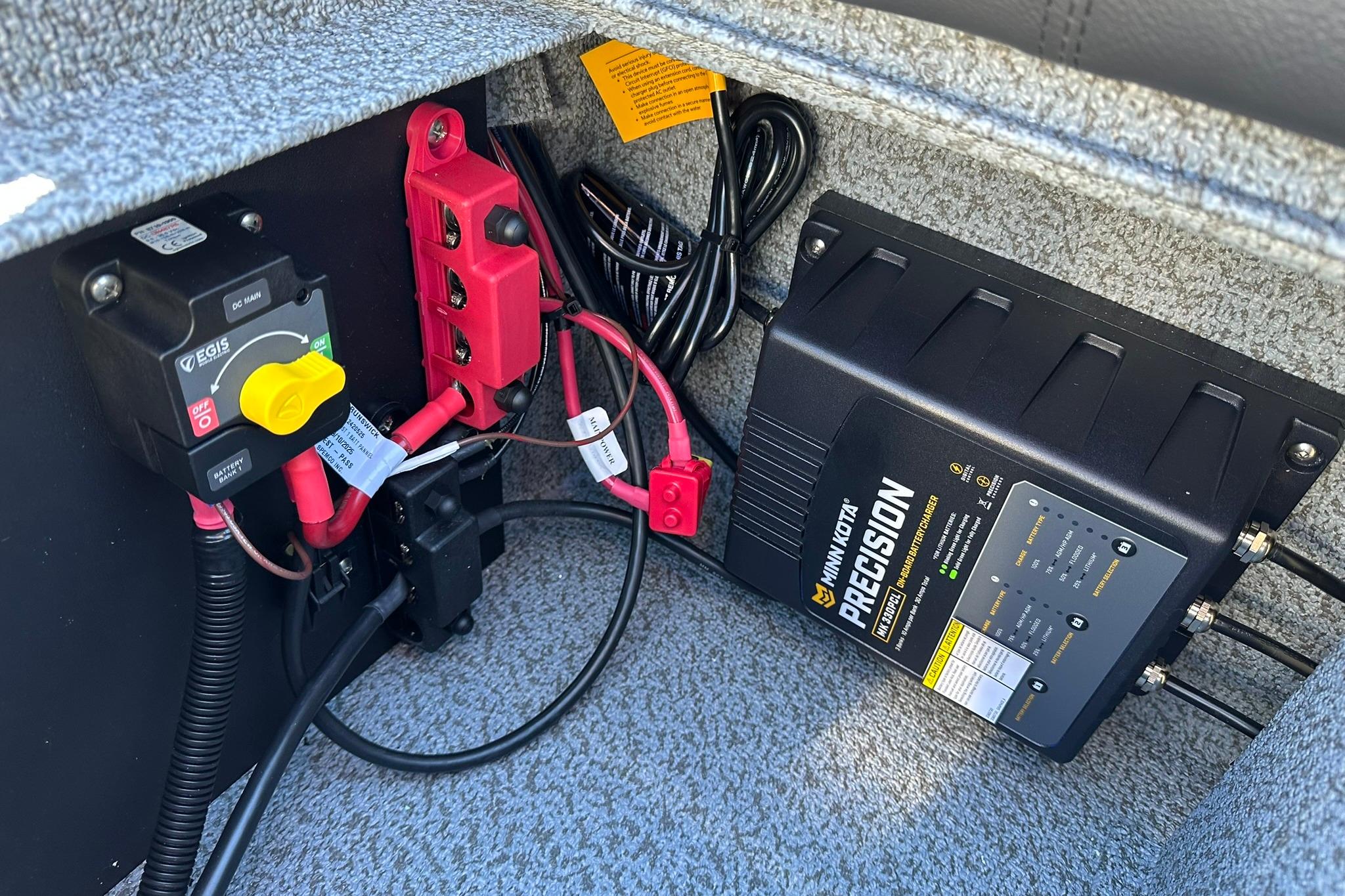 Electrical components inside a 2026 Lund 1875 Impact XS Sport boat, featuring a Minn Kota Precision charger.