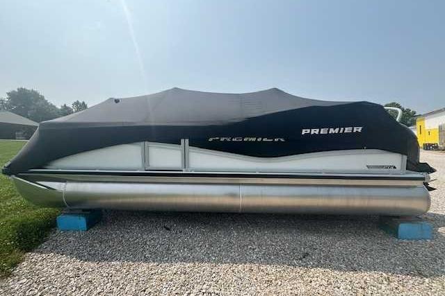 2025 Premier 220 SUNSCAPE RL pontoon boat covered, resting on gravel with blue supports.