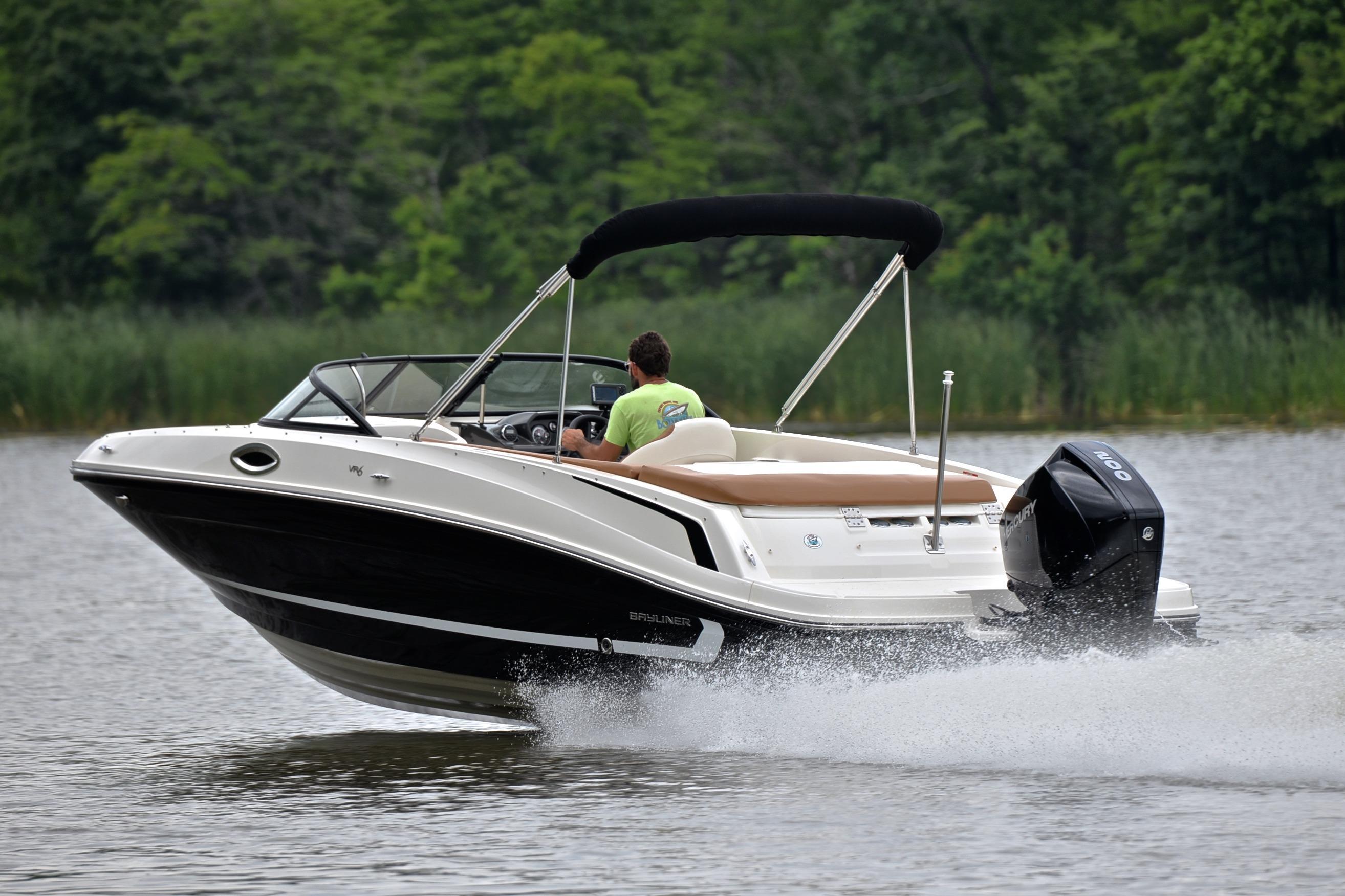 2019 Bayliner VR6 Bowrider OB cruising on a lake with lush green background.
