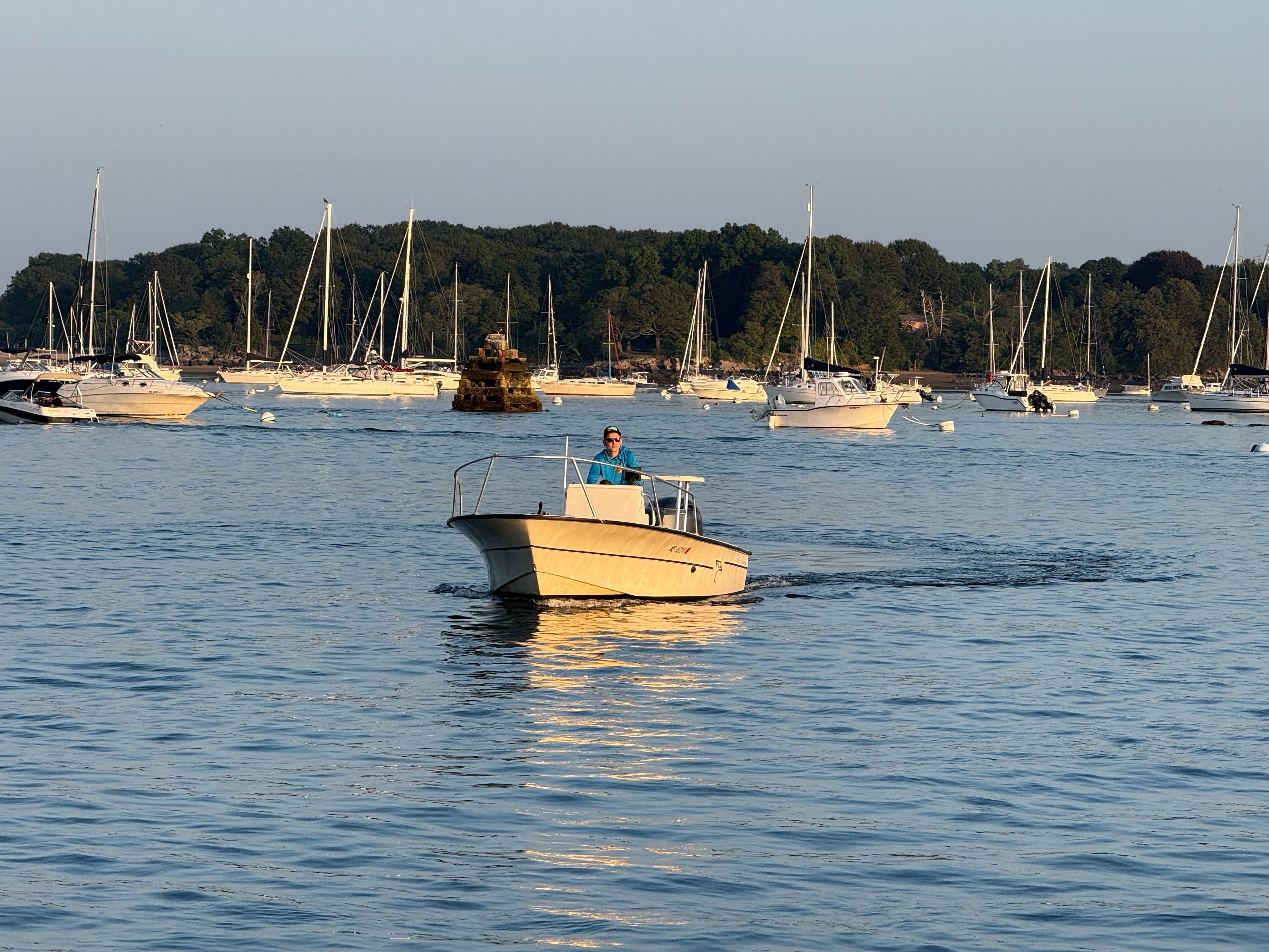 Small boat "Sea Fly" 2004 on calm water, surrounded by sailboats and lush greenery.