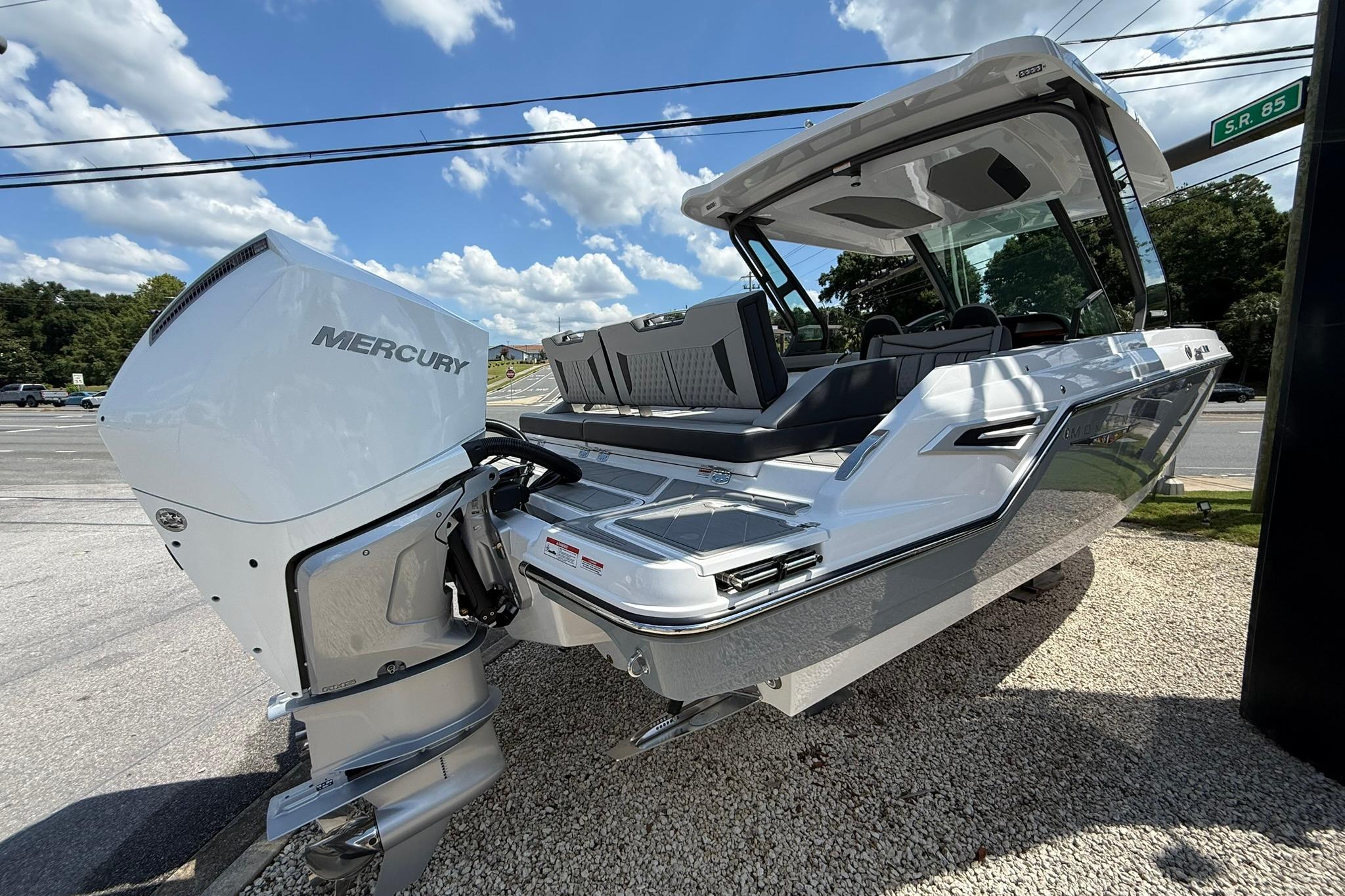 2027 Monterey Elite 30 OB boat with Mercury outboard engine, parked on gravel under a blue sky.