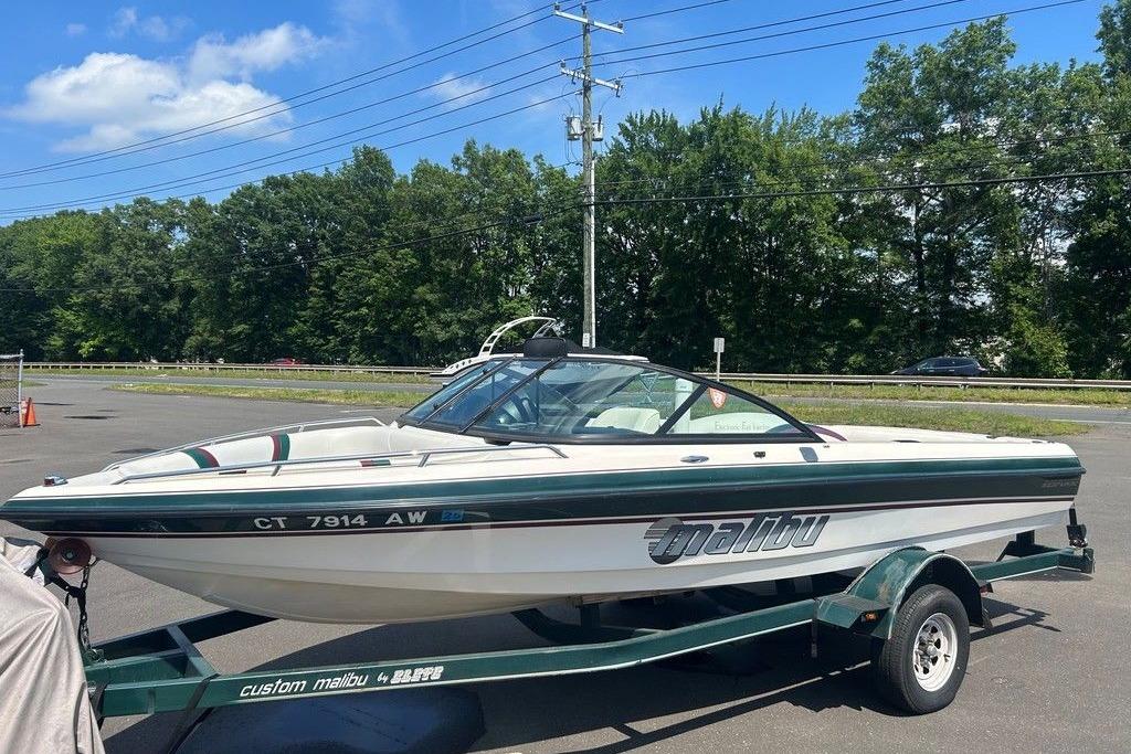 1999 Malibu Response boat on trailer, parked outdoors under a clear sky.