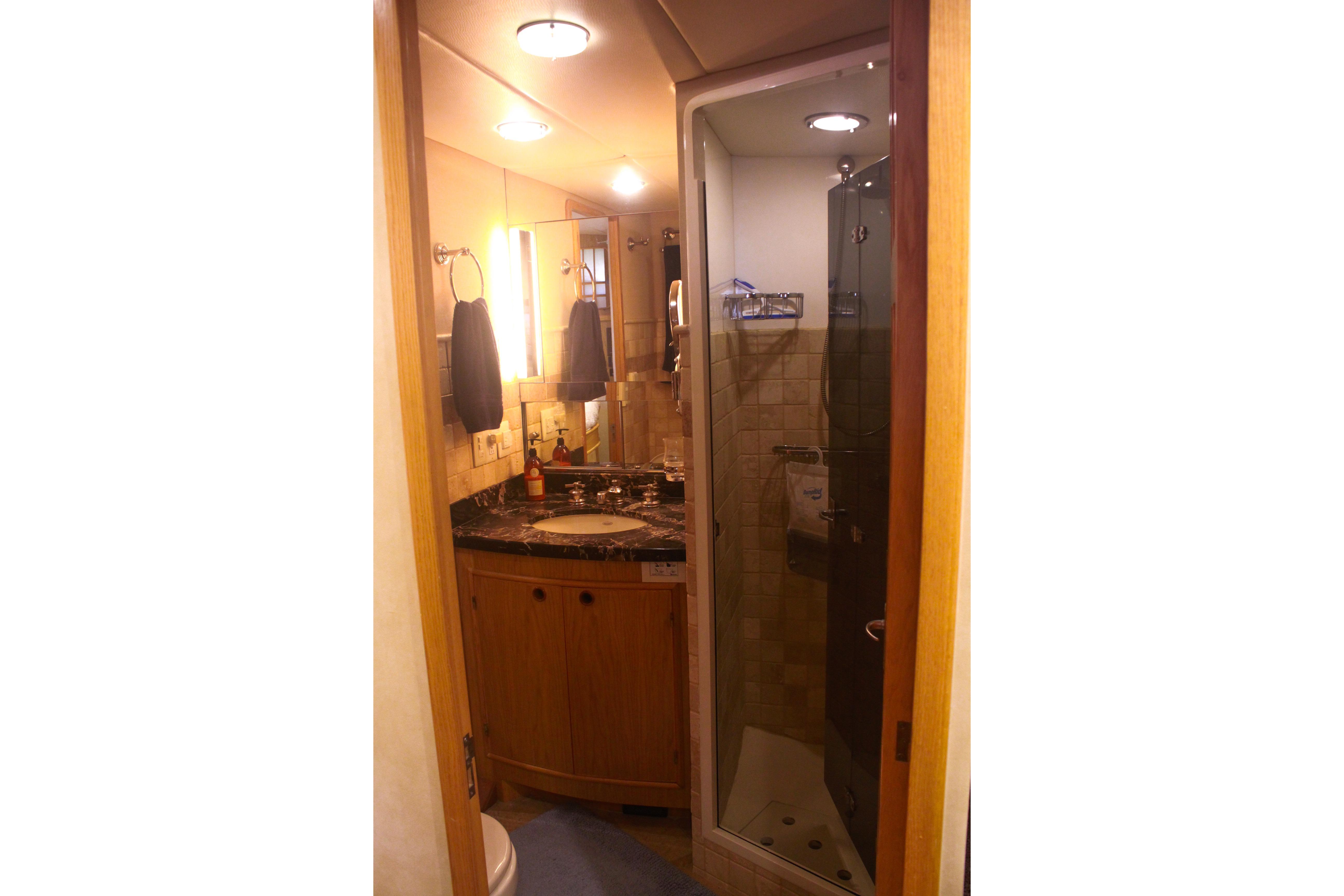 1999 Grand Alaskan Pilothouse bathroom with wooden cabinetry, marble countertop, and glass shower.