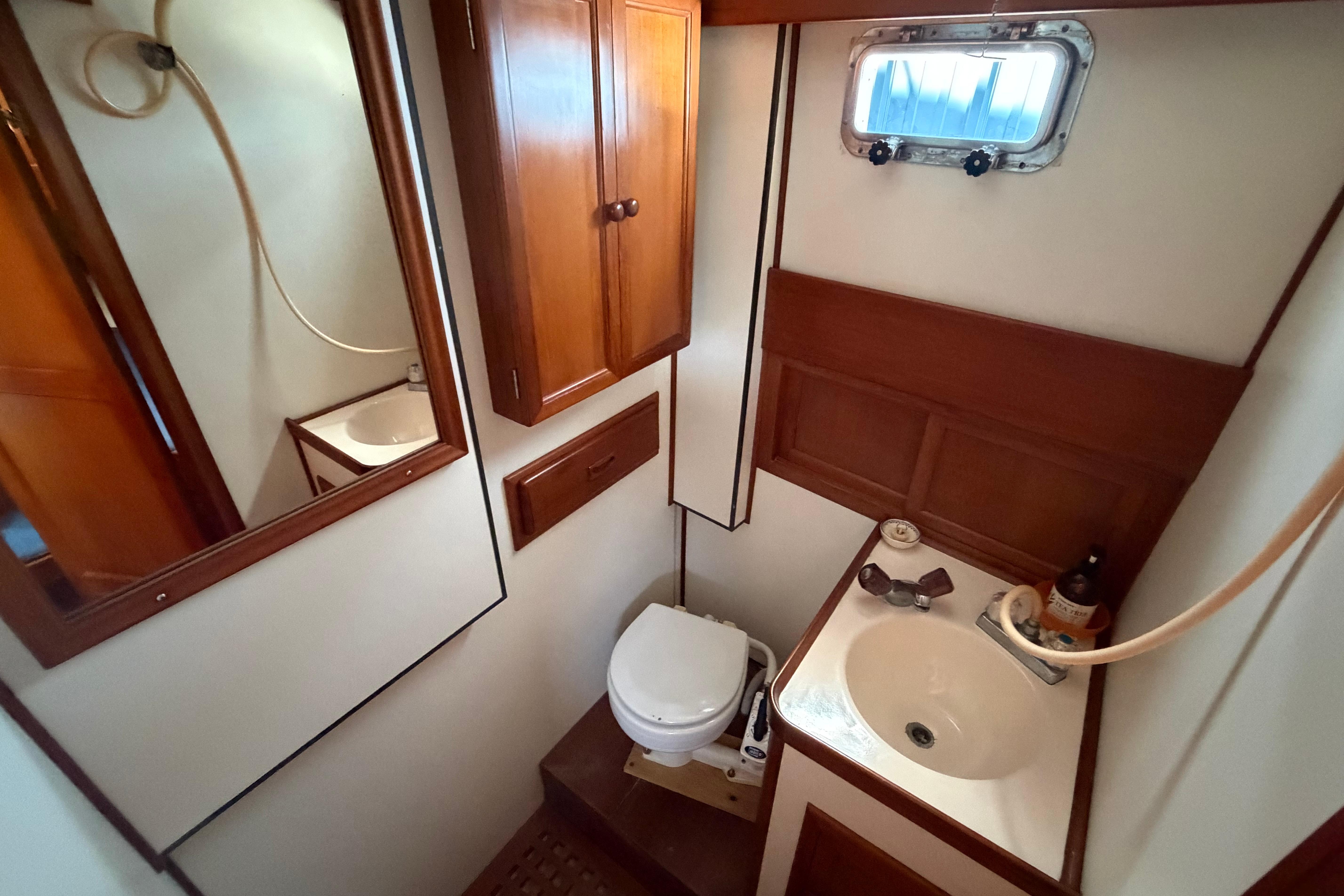 1987 Marine Trader 36 bathroom with wooden cabinets, sink, and porthole window.