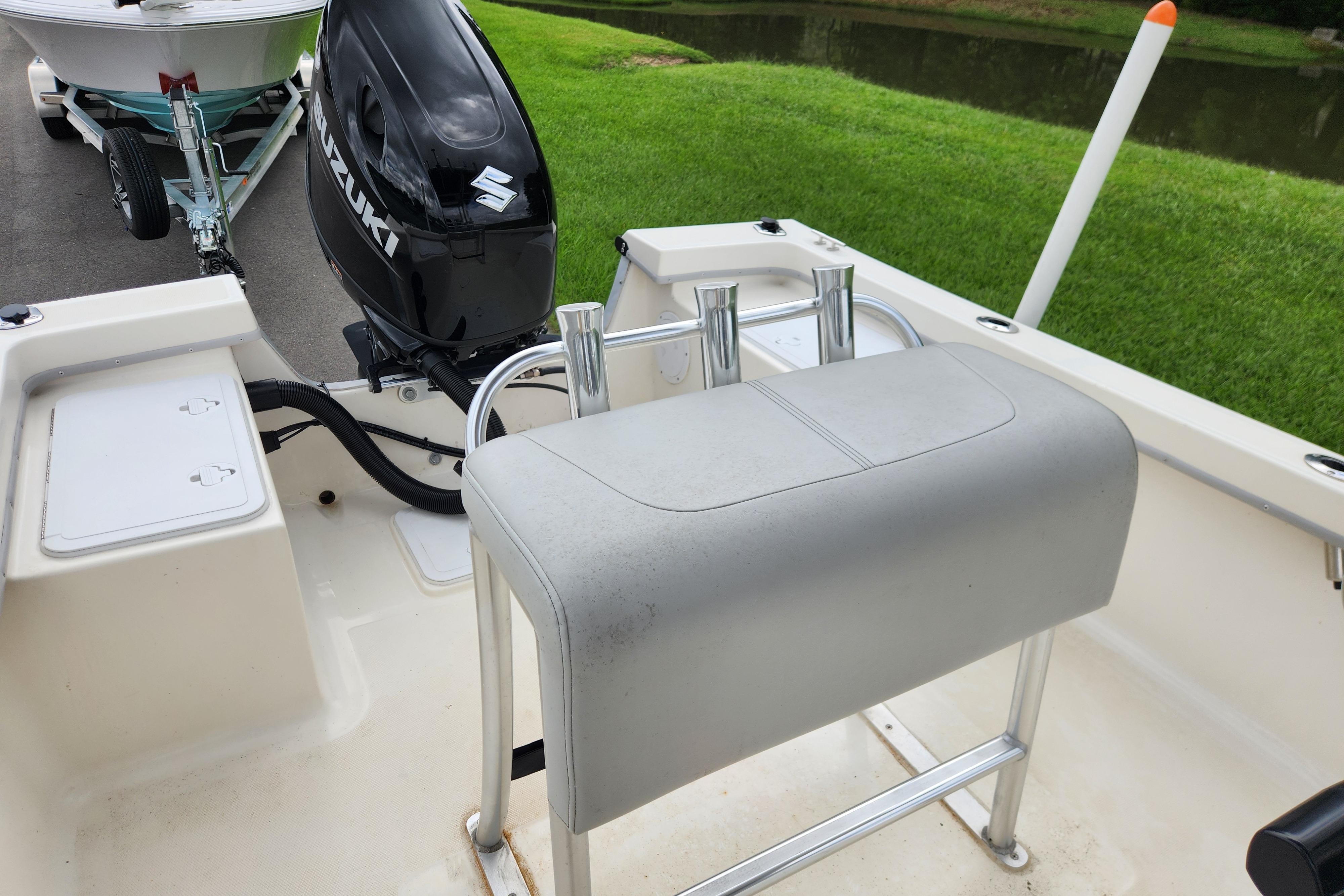 2023 May-Craft 1900CC boat interior with Suzuki outboard motor, near grassy waterway.