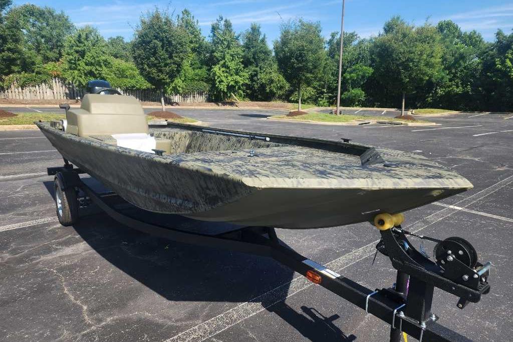 2026 Tracker Grizzly 1648 SC boat on trailer in parking lot, surrounded by trees.