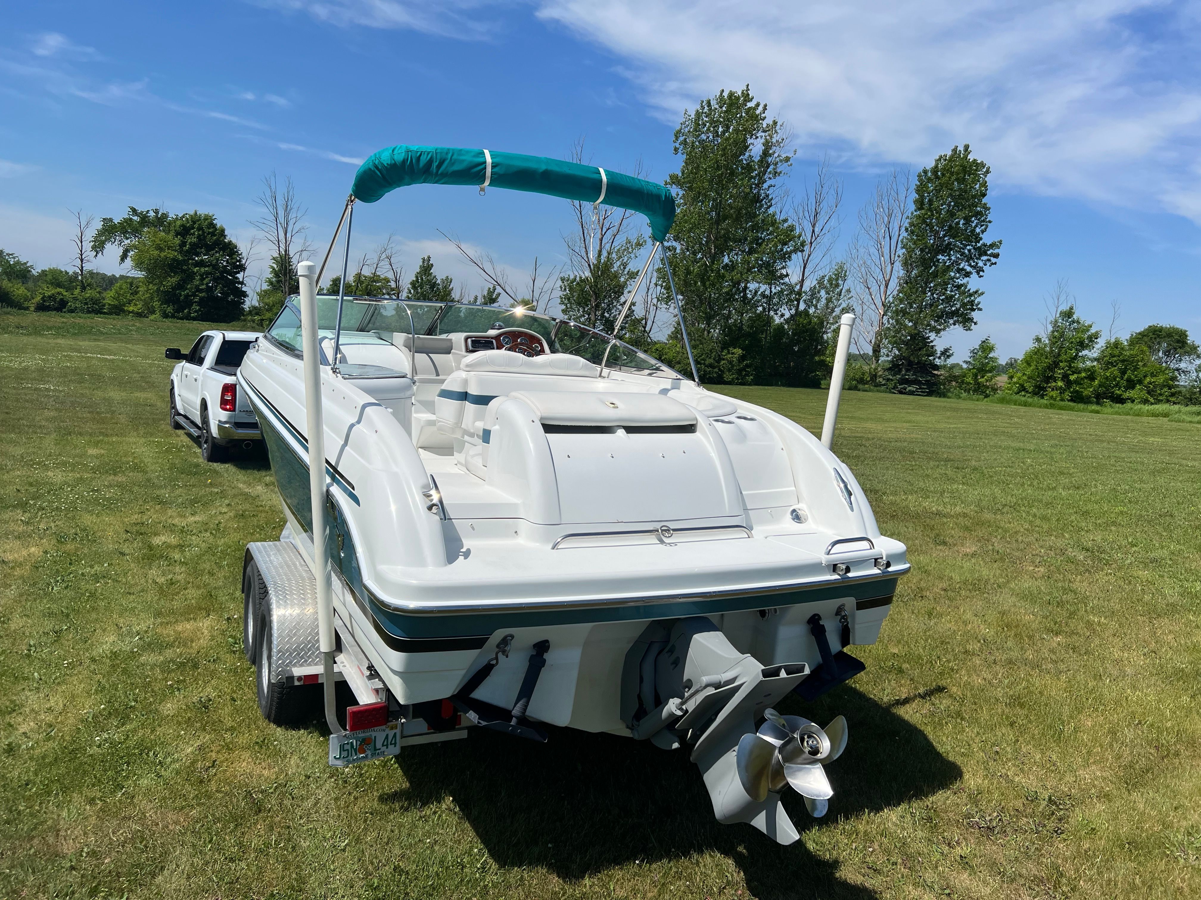 A white motorboat on a trailer in a grassy field, with a car in the background.