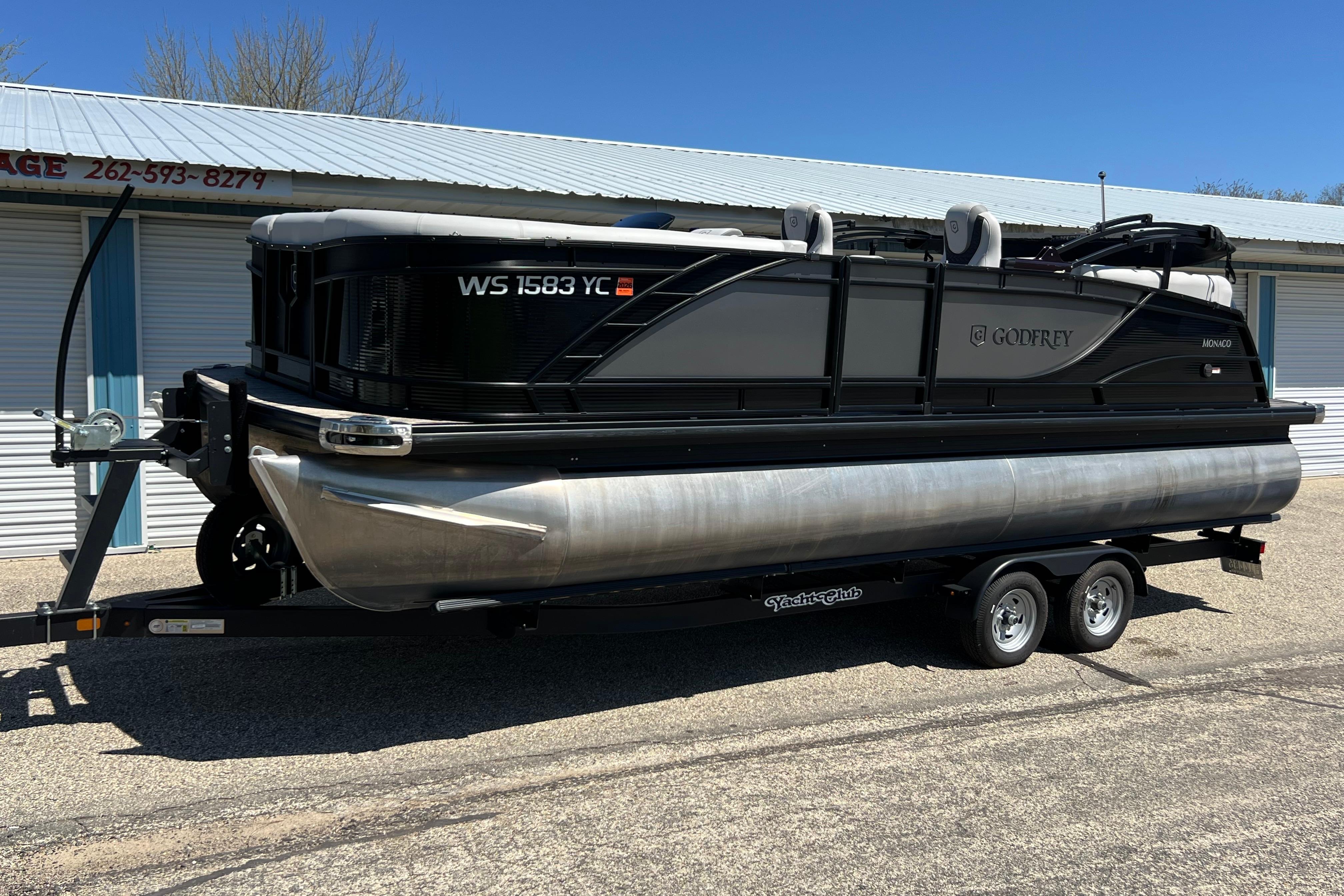 2023 Godfrey Monaco 235 SB pontoon boat on trailer, parked outdoors.