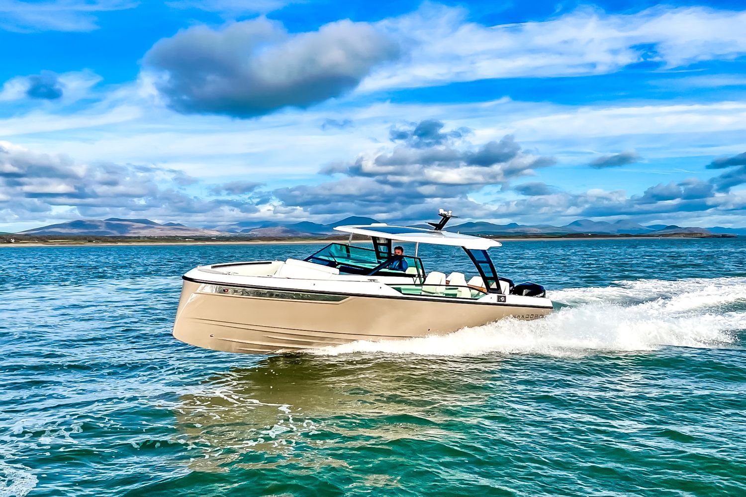 A modern motorboat speeds across the water under a blue sky.