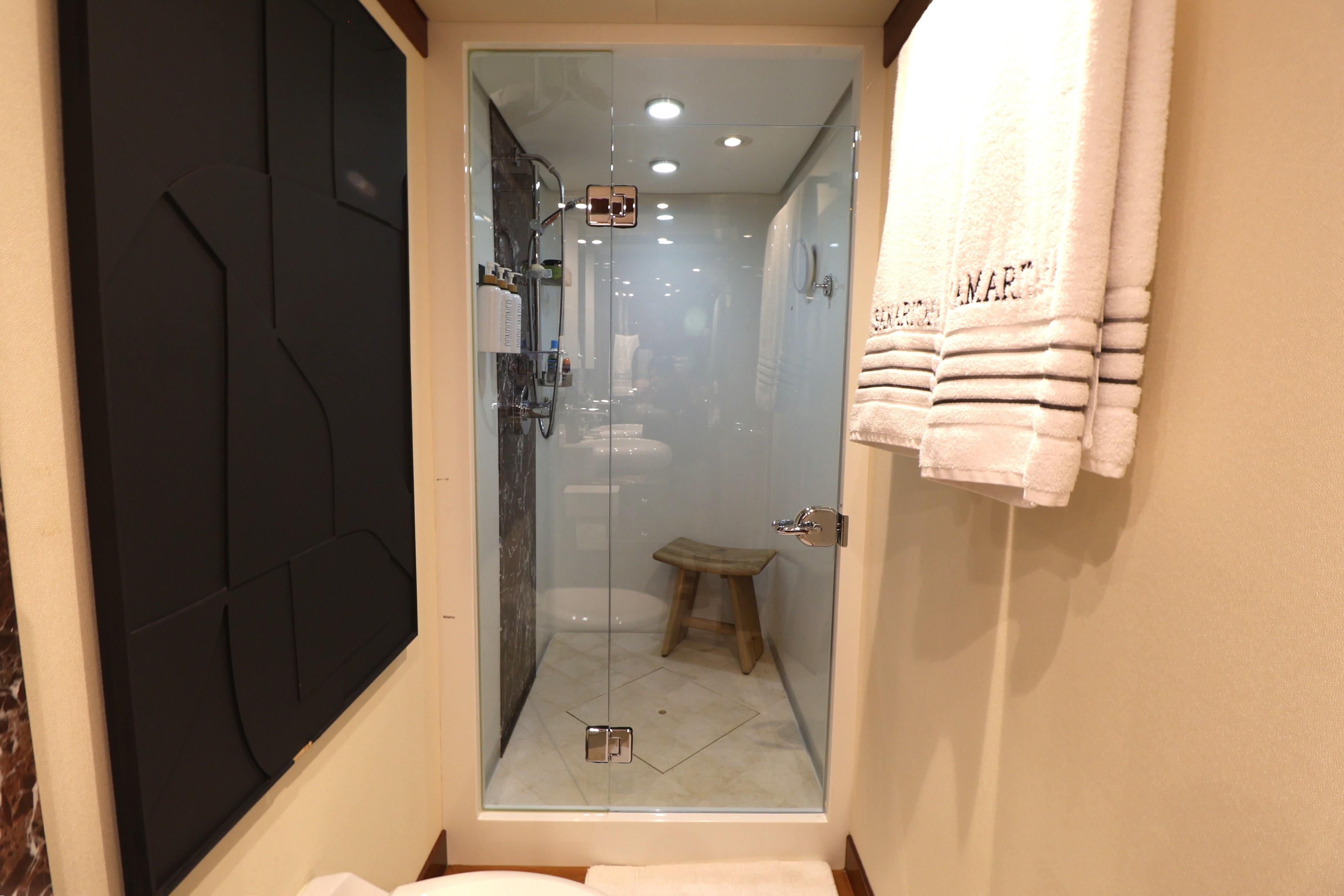 Luxurious bathroom shower in 2013 Cheoy Lee Bravo yacht with glass door and wooden stool.