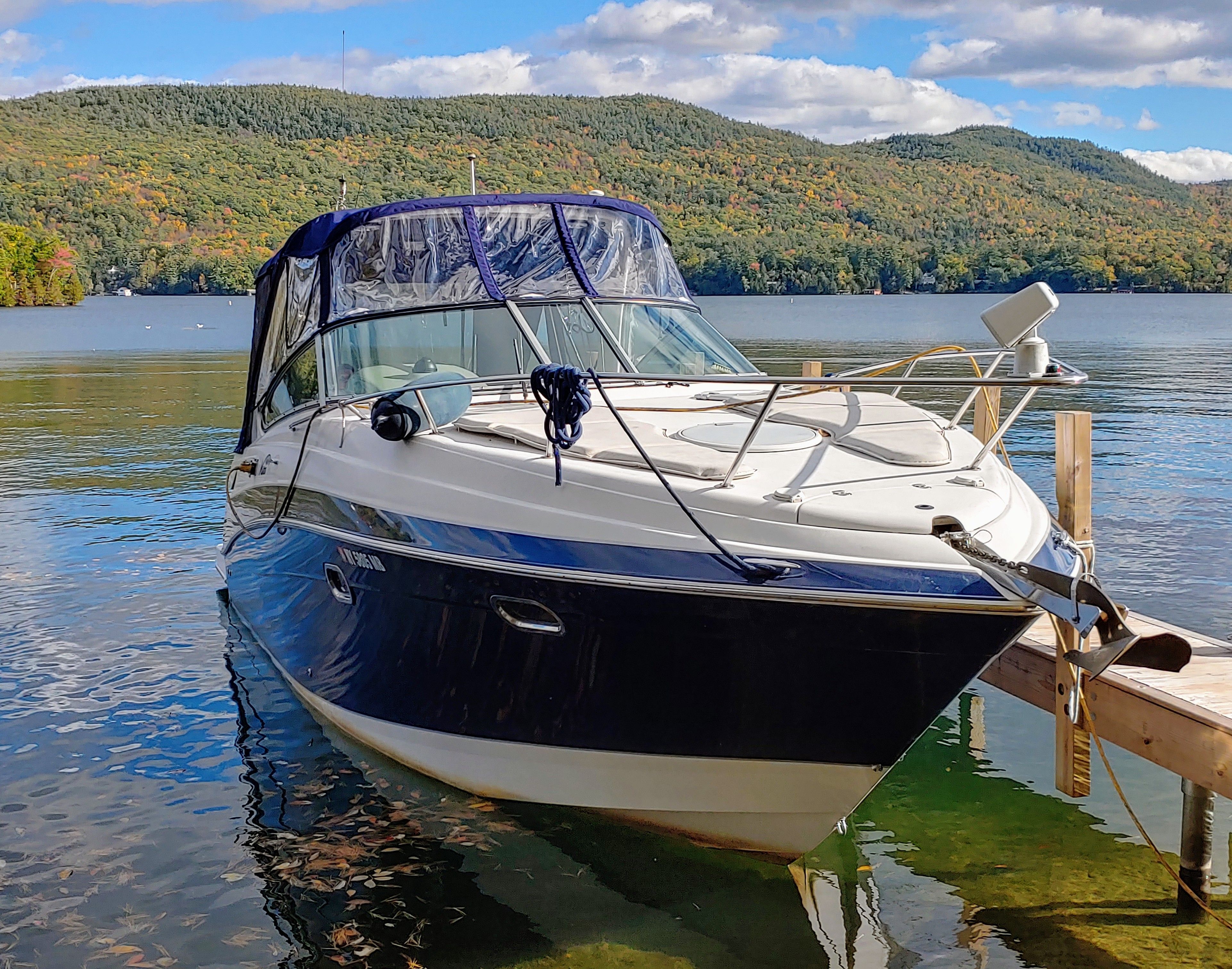 A boat docked at a pier on a calm lake with wooded hills in the background.