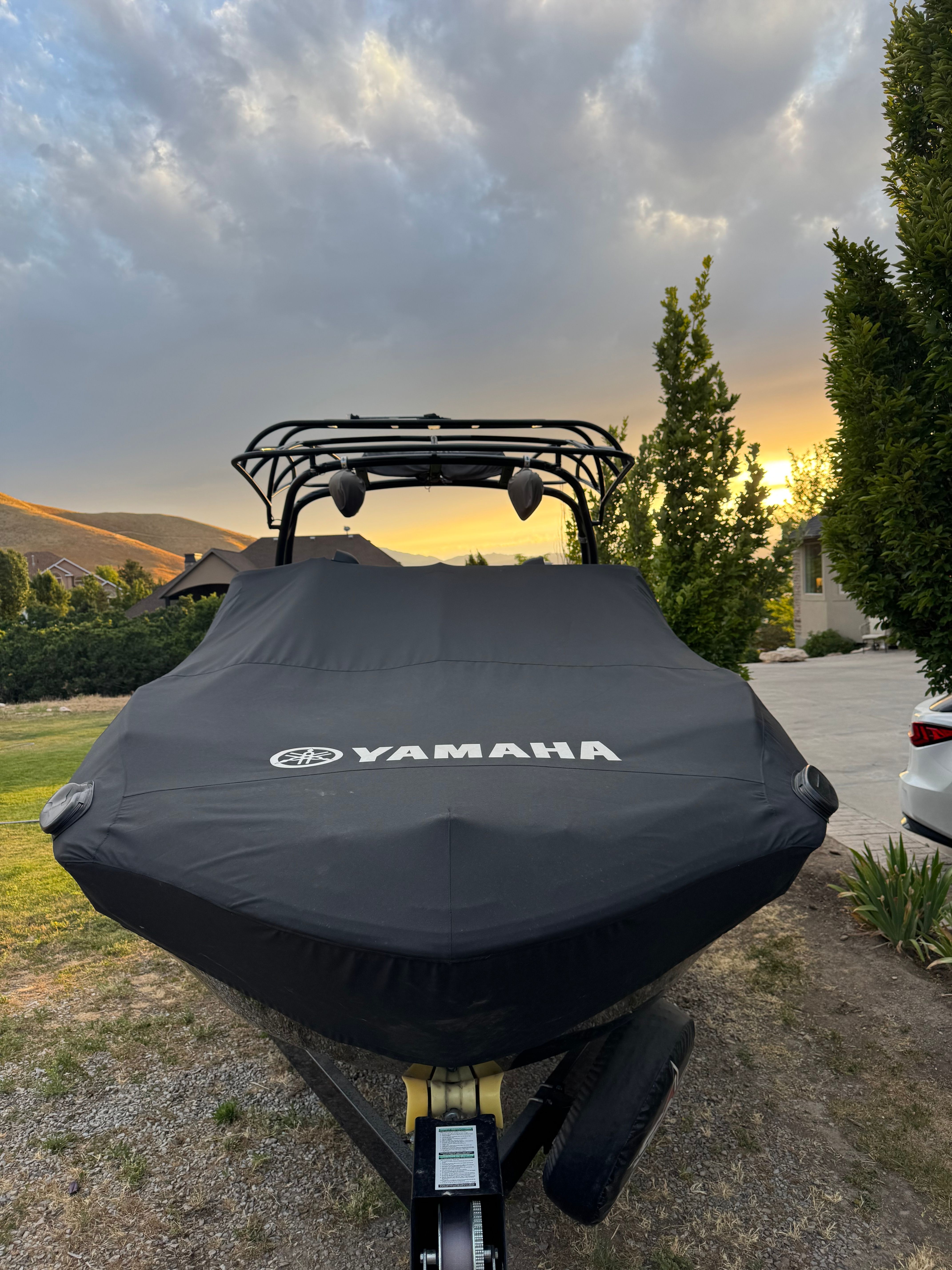 A Yamaha boat with a cover sits on a trailer, surrounded by trees and a sunset.