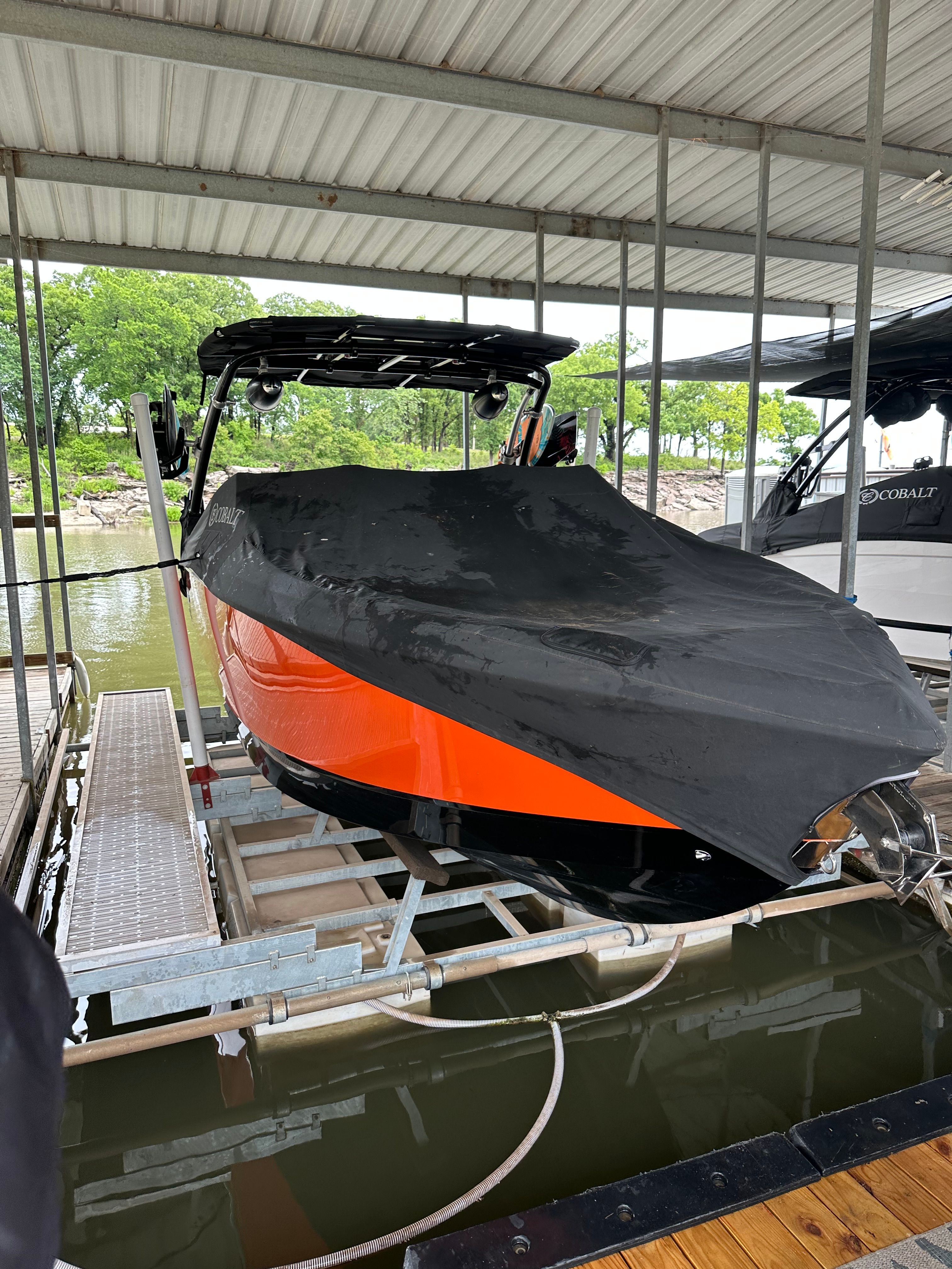 A 2019 Cobalt R7 Surf boat with a black cover is docked in a covered slip.