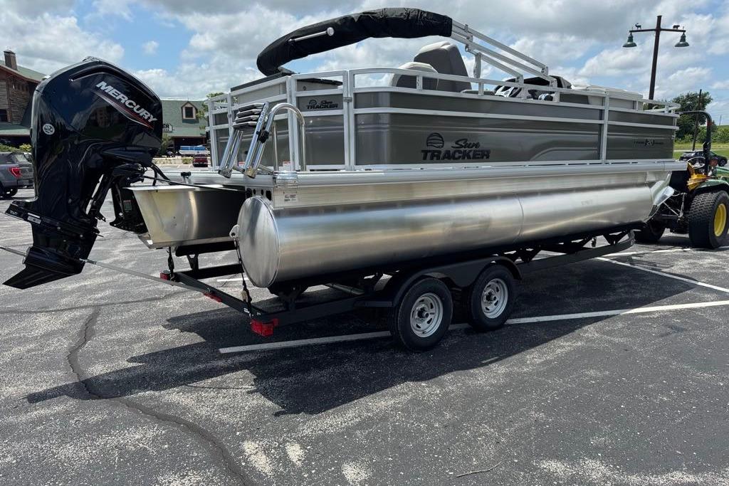 2026 Sun Tracker Fishin' Barge 20 DLX pontoon boat on trailer in parking lot.
