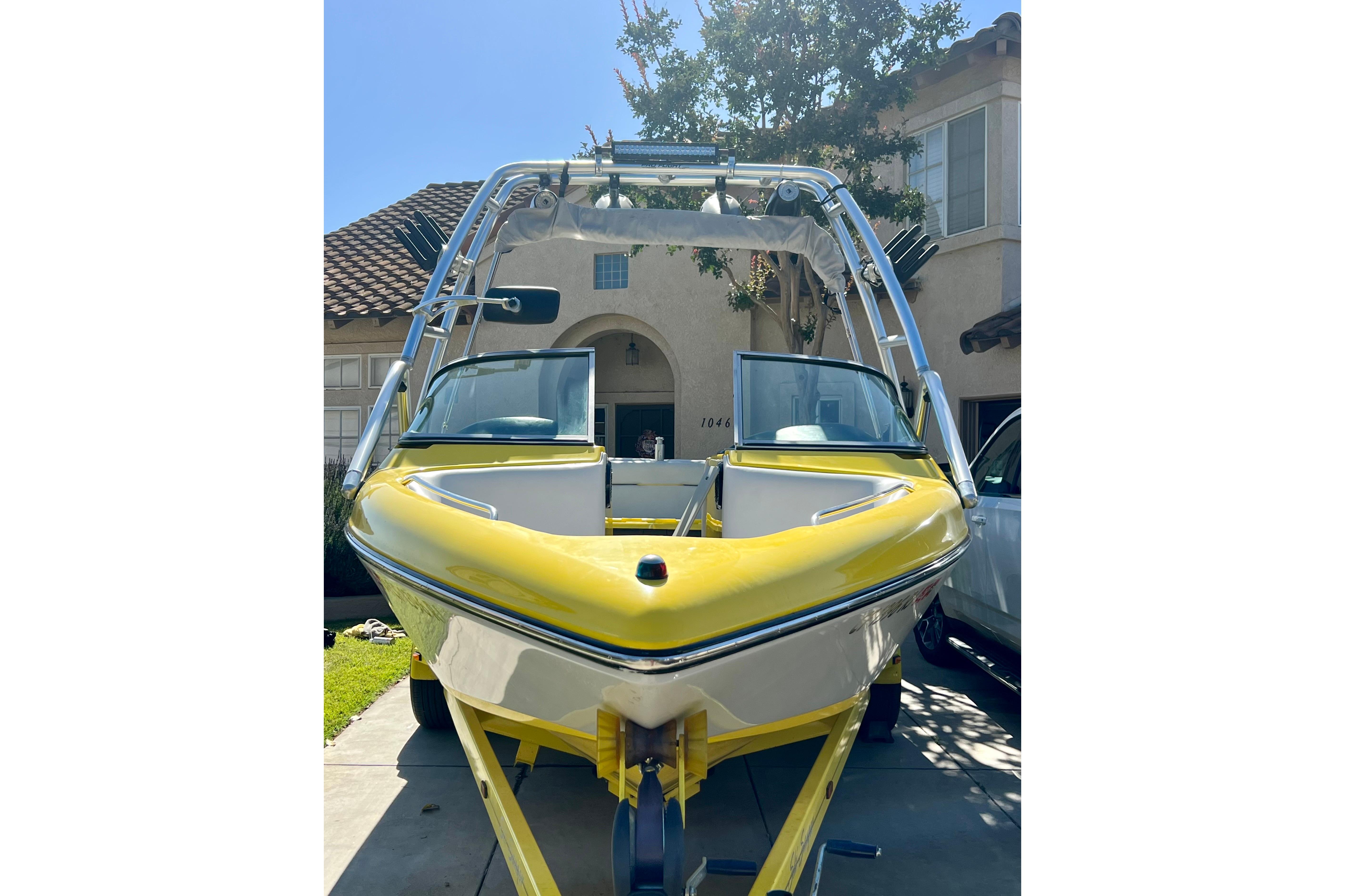 Yellow 2006 Sanger V230 boat parked in driveway, featuring sleek design and wakeboard tower.