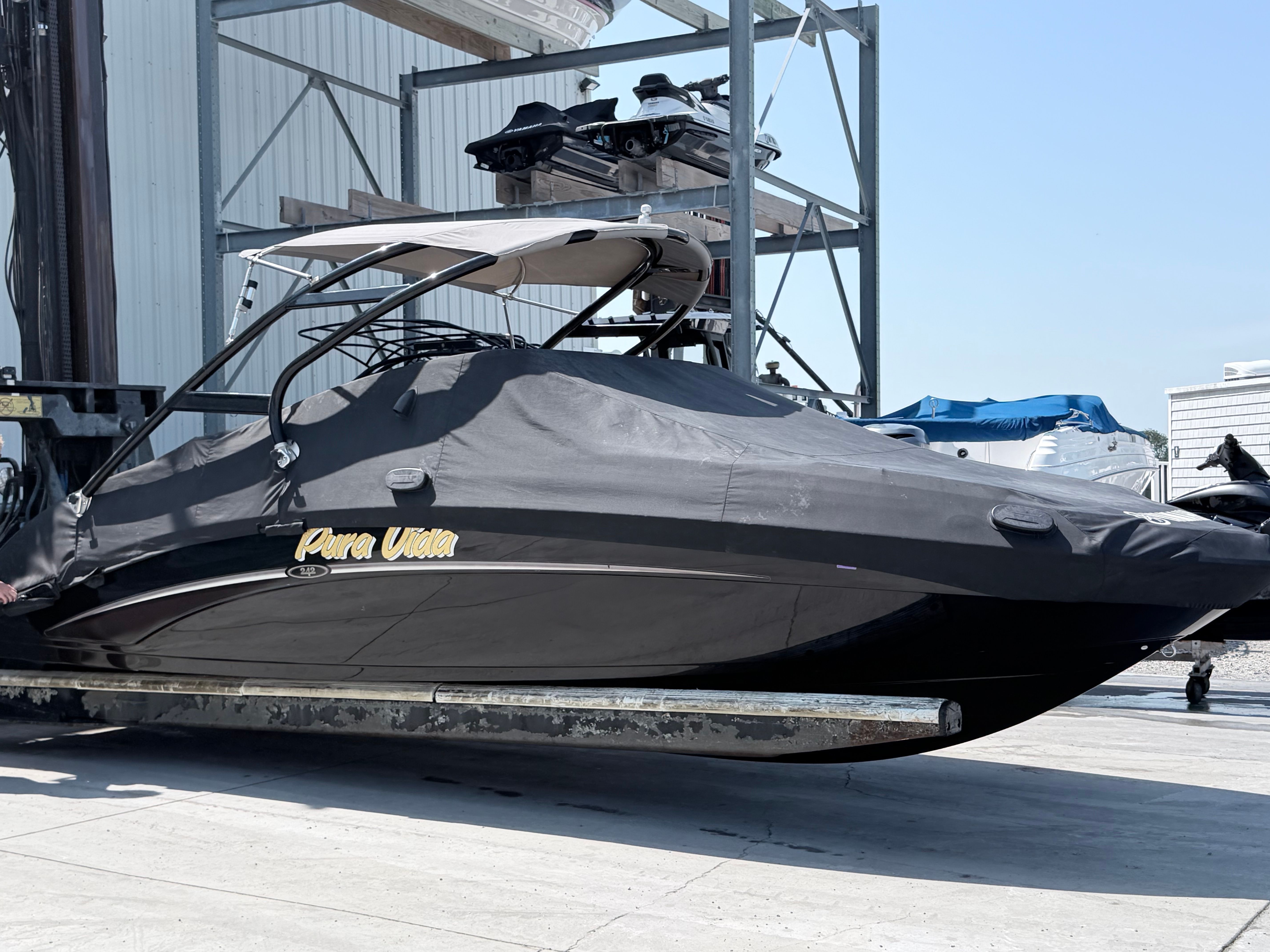 A 2014 Yamaha 242 Limited S boat with a cover, on a trailer in a storage area.