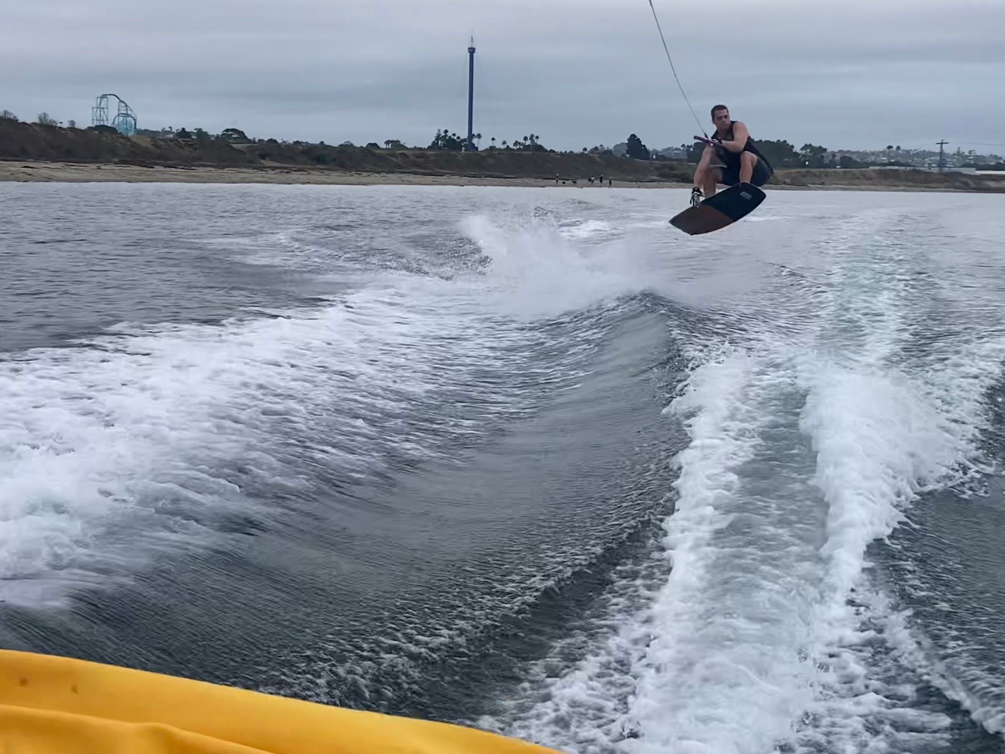 A wakeboarder jumps over waves behind a boat on a lake.