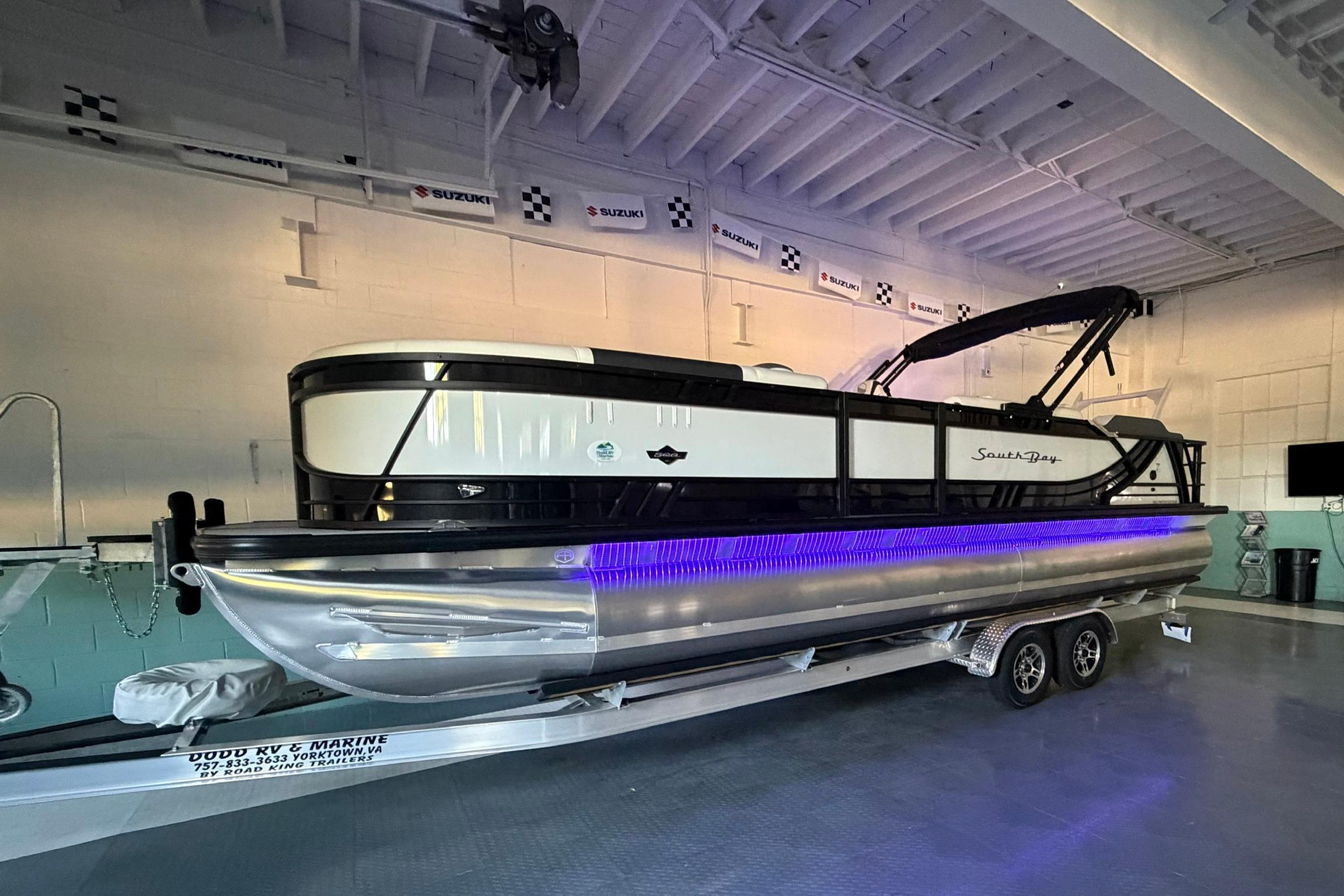 2026 South Bay 525SB2 pontoon boat with blue LED lights on trailer indoors.