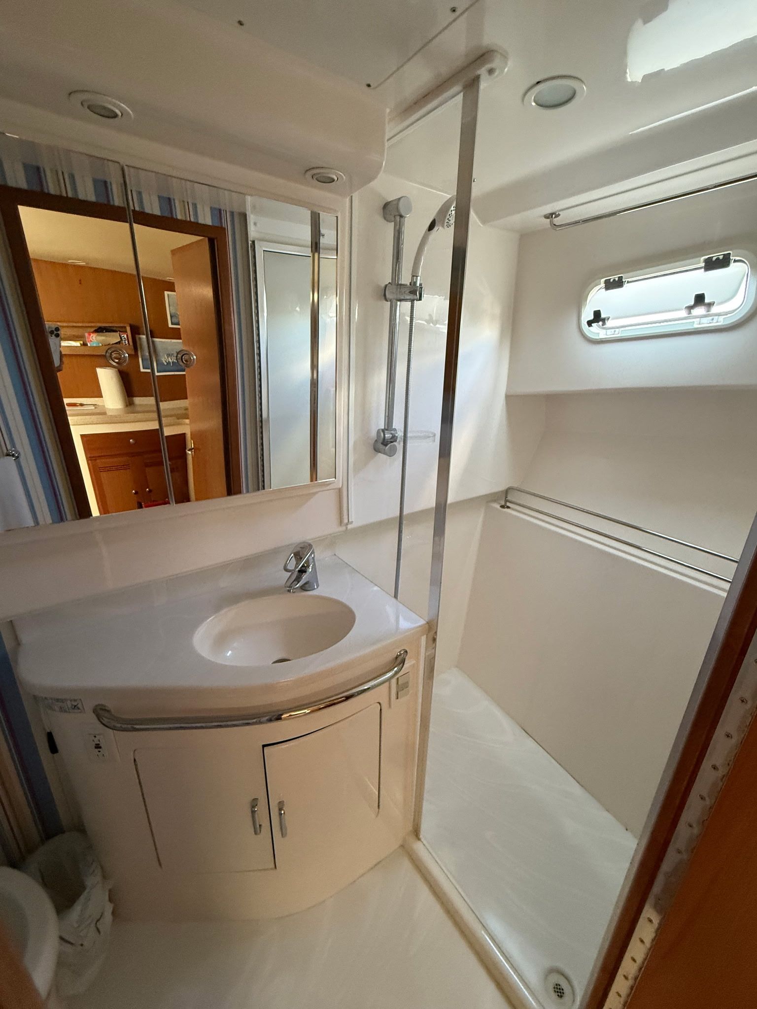 The image shows a boat bathroom with a shower, sink, and mirror.