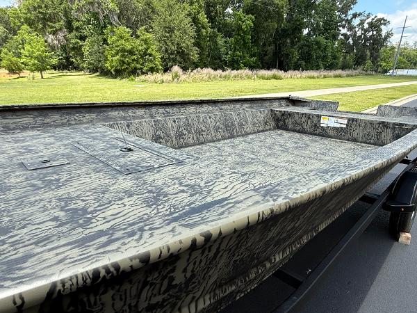 2025 Tracker GRIZZLY 2072 Utility boat with camouflage design on a trailer, surrounded by greenery.