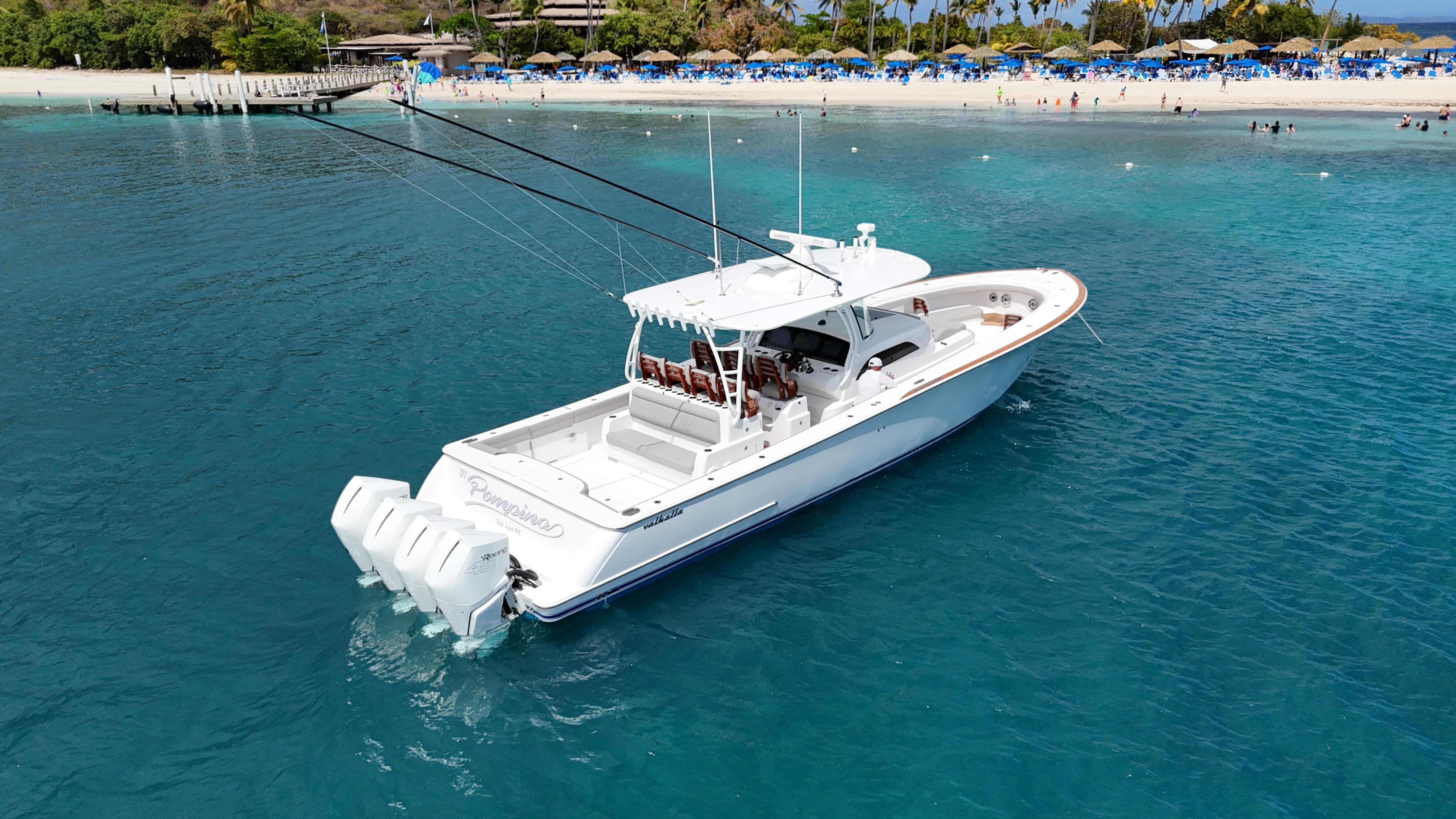 2023 Valhalla Boatworks V-46 cruising in clear blue waters near a sandy beach.