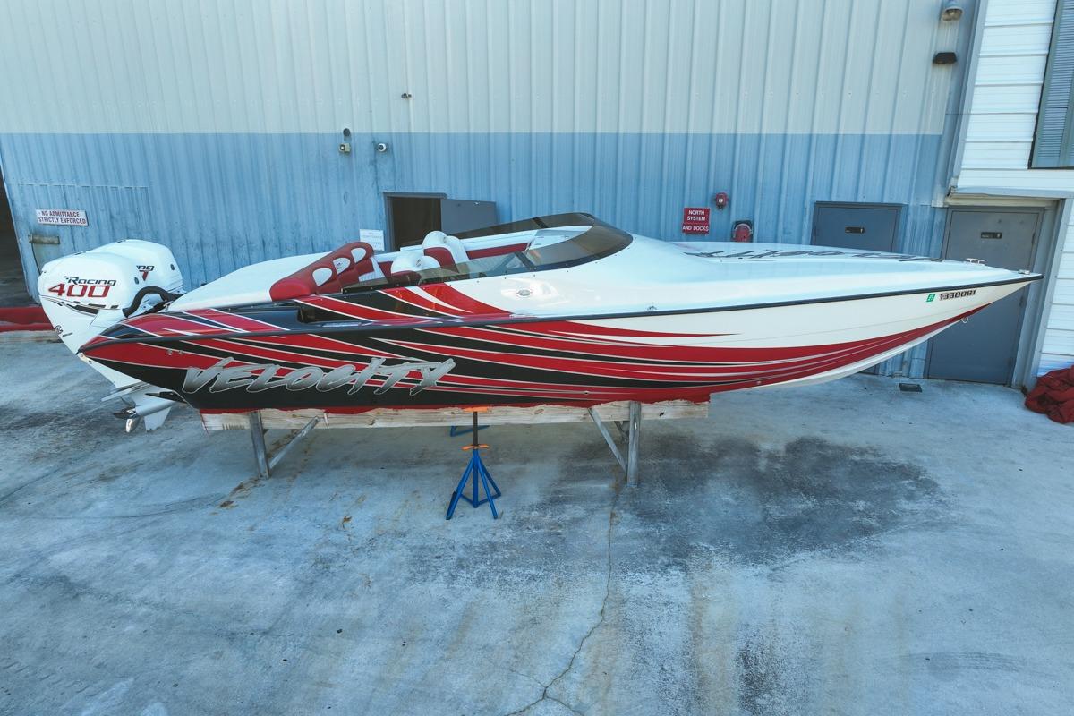 2022 Velocity 290sc speedboat with red and black graphics, parked outside a warehouse.