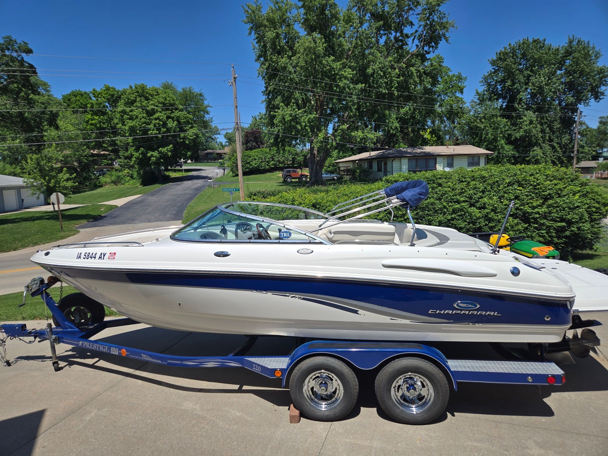 A white 2005 Chaparral 220 SSi boat on a blue trailer, parked in a residential area.