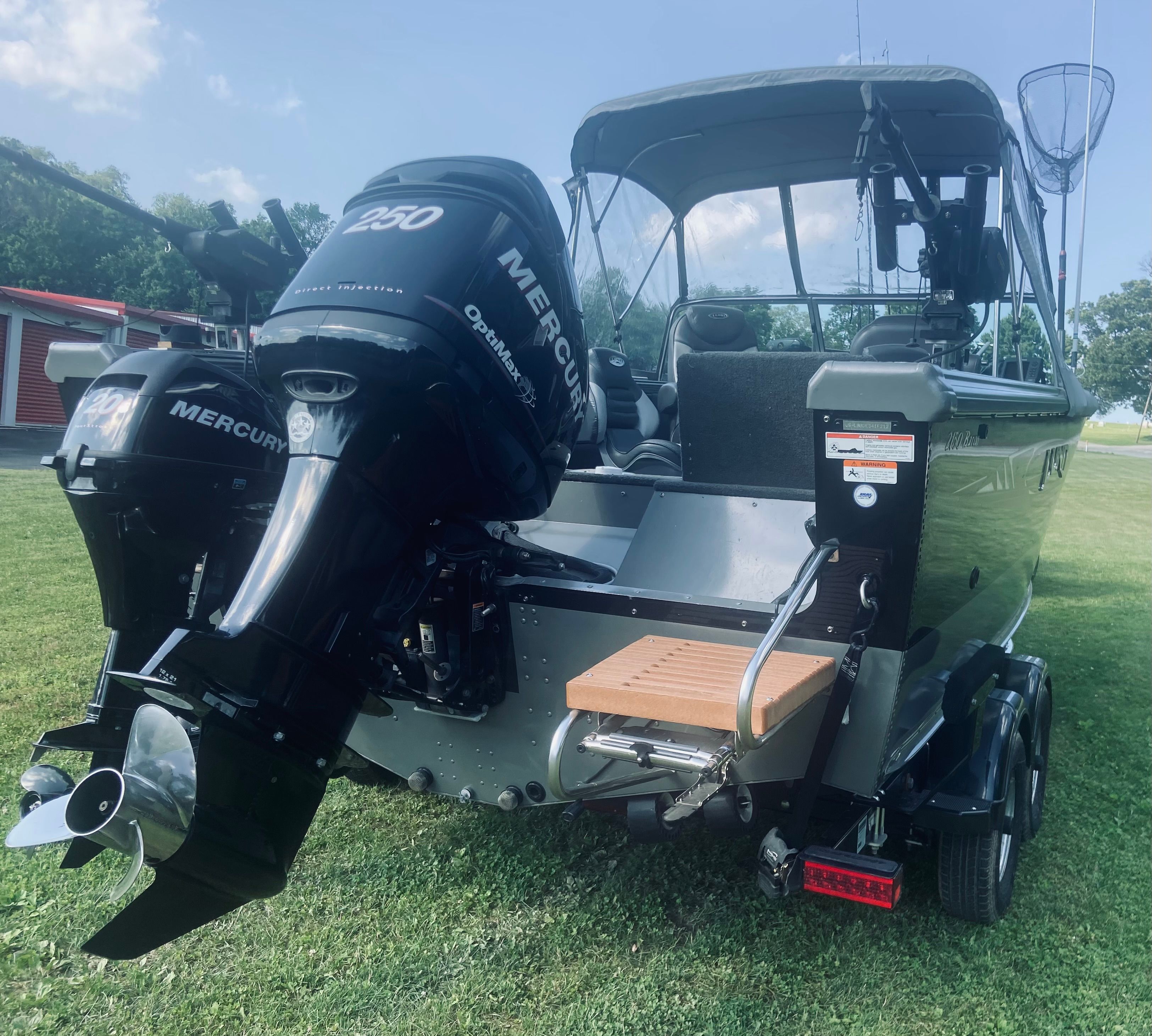 A 2012 Lund Baron boat with a Mercury outboard motor, parked on a trailer on grass.