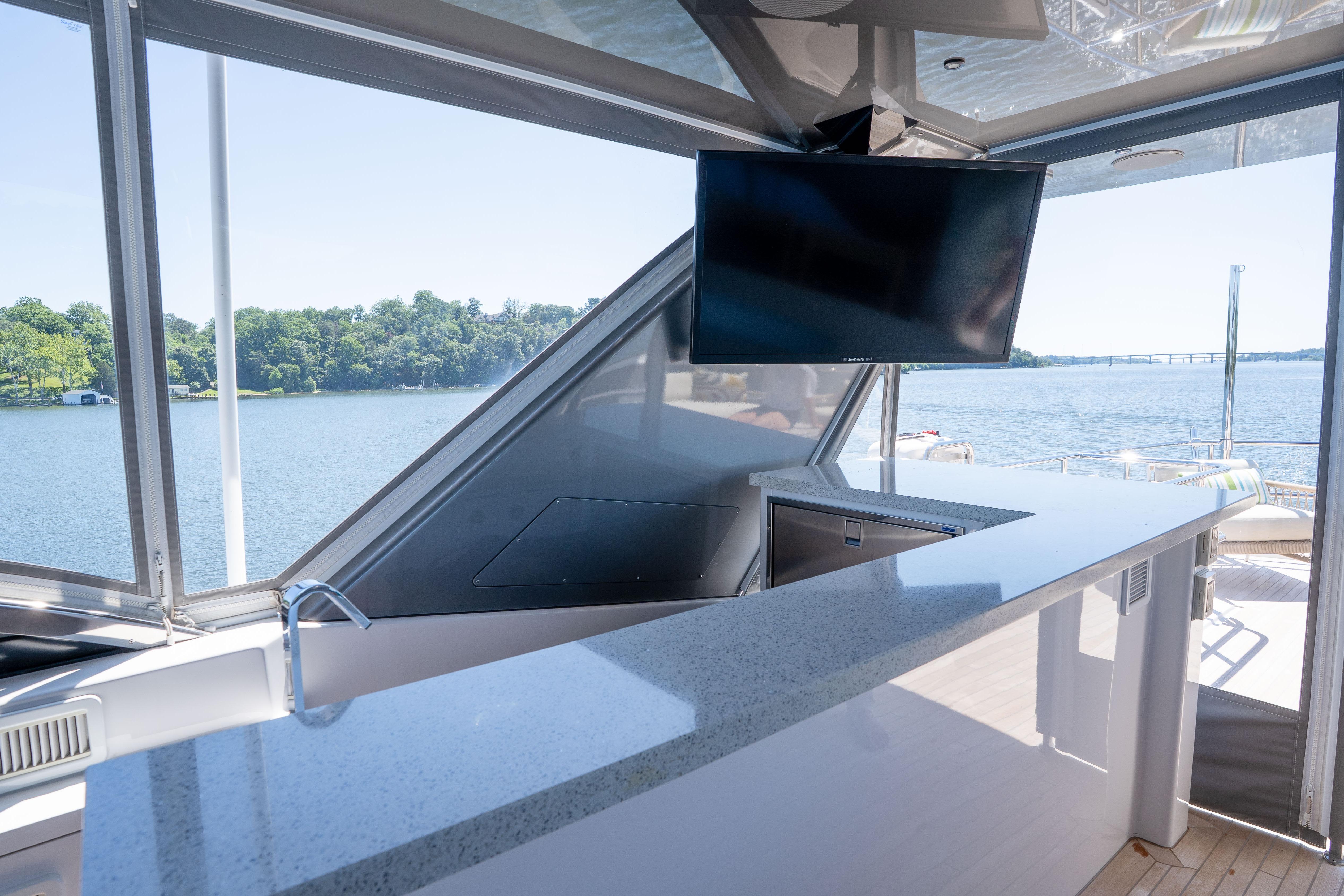 Luxurious 2021 Hatteras M75 Panacera yacht bar with TV, overlooking serene waters.