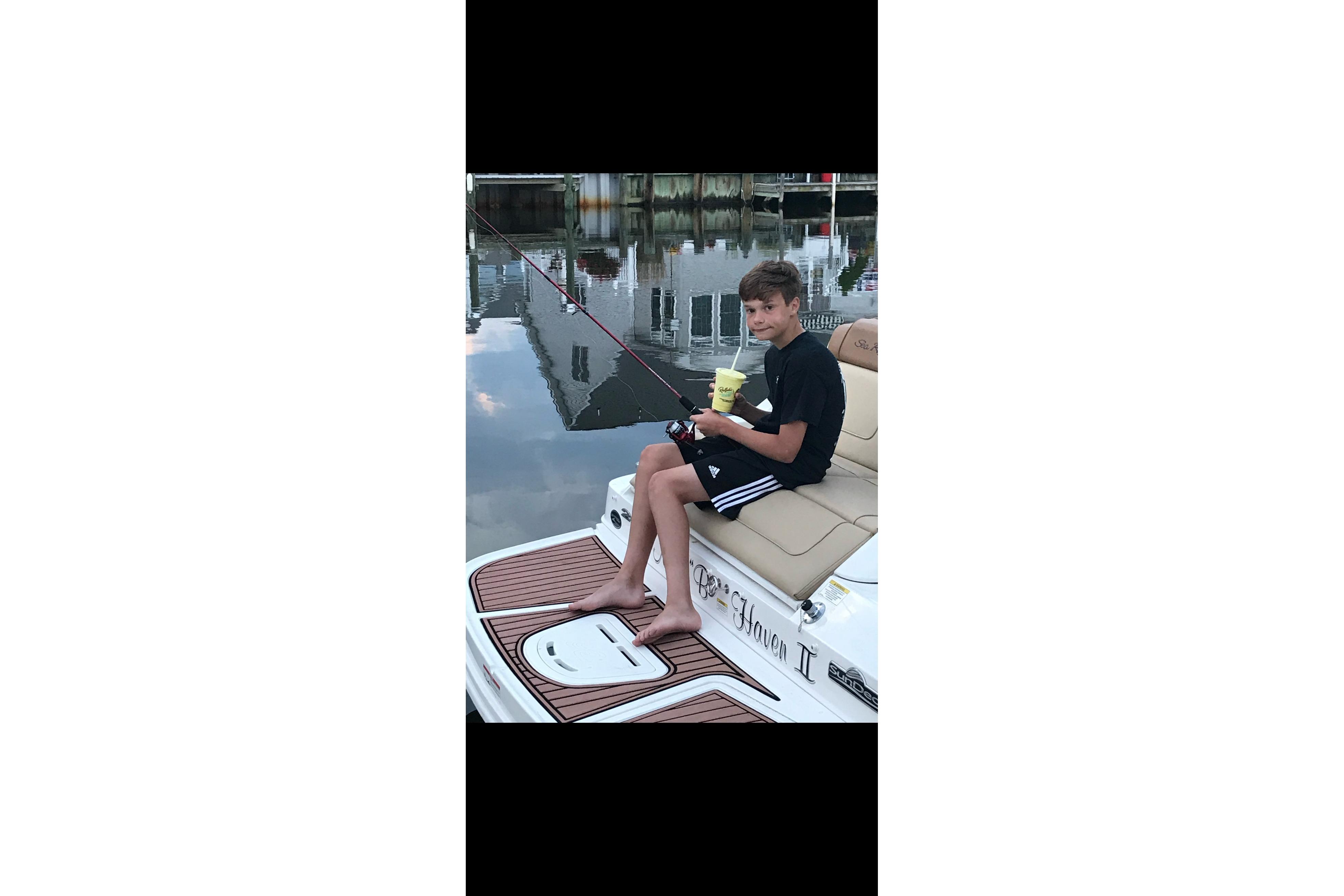 Young person relaxing on a 2014 Sea Ray 260 Sundeck, holding a drink by the water.