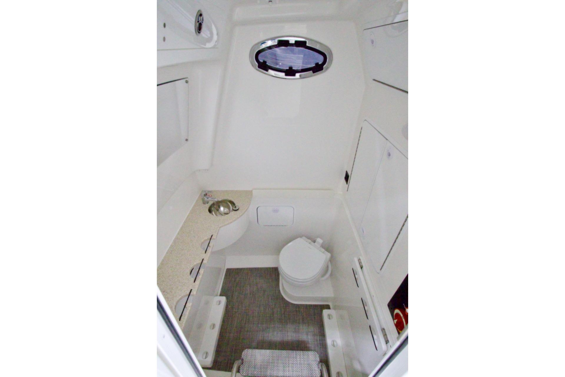 2026 Regulator 31 boat interior with compact bathroom, featuring a toilet, sink, and storage cabinets.