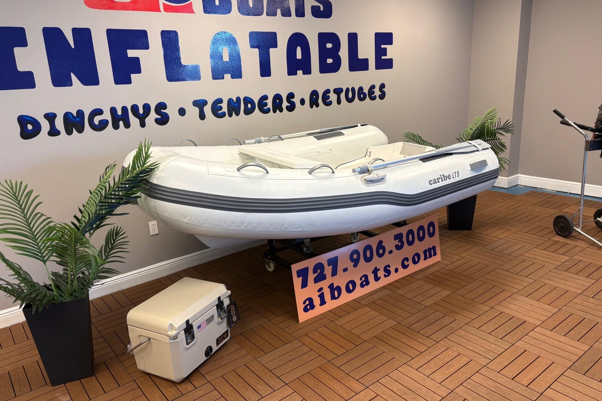 Inflatable Caribe L-9 boat displayed indoors, 2025 model, with contact information and decorative plants.