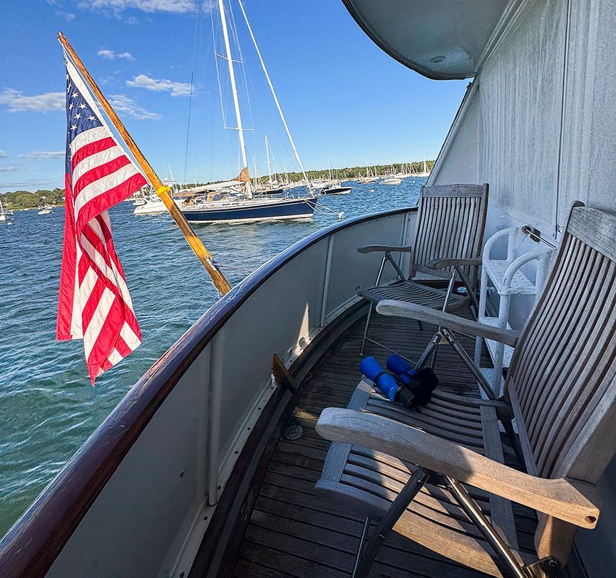 A 1961 Burger 63 with wooden chairs on deck, overlooking the water and a flag.