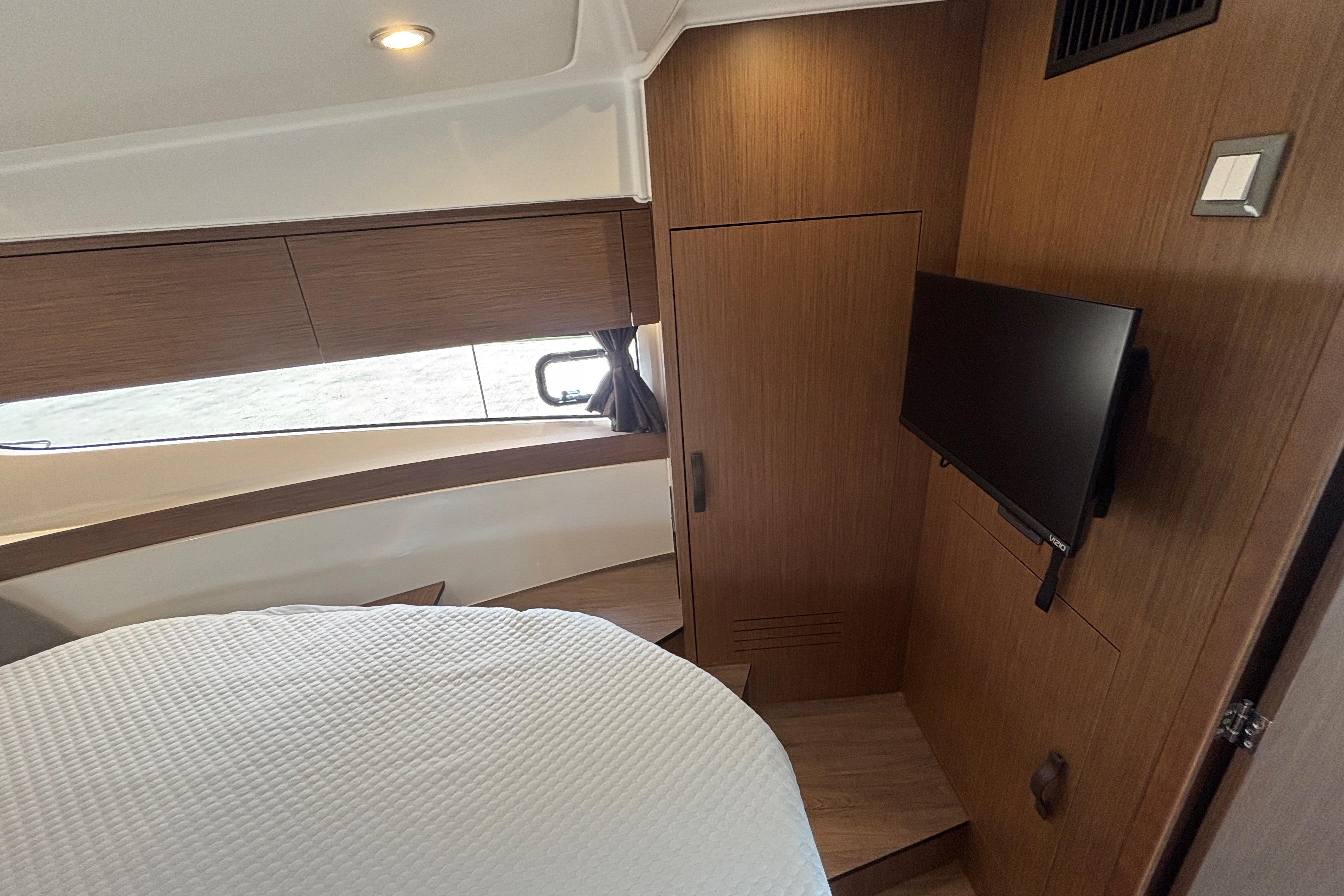 2024 Beneteau Antares 11 cabin interior with bed, TV, and wooden cabinetry.