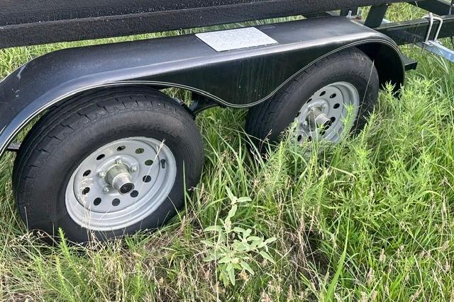 Trailer wheels of a 2019 Sun Tracker Party Barge 22 XP3 in grassy area.