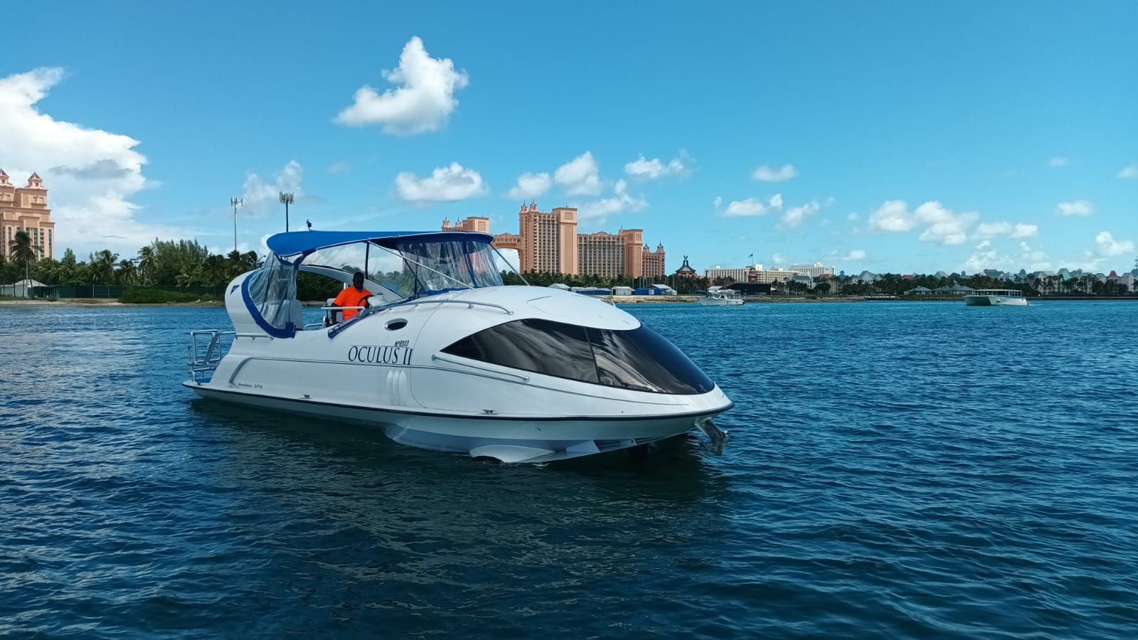 A modern glass-bottom boat cruises on calm water with a cityscape in the background.