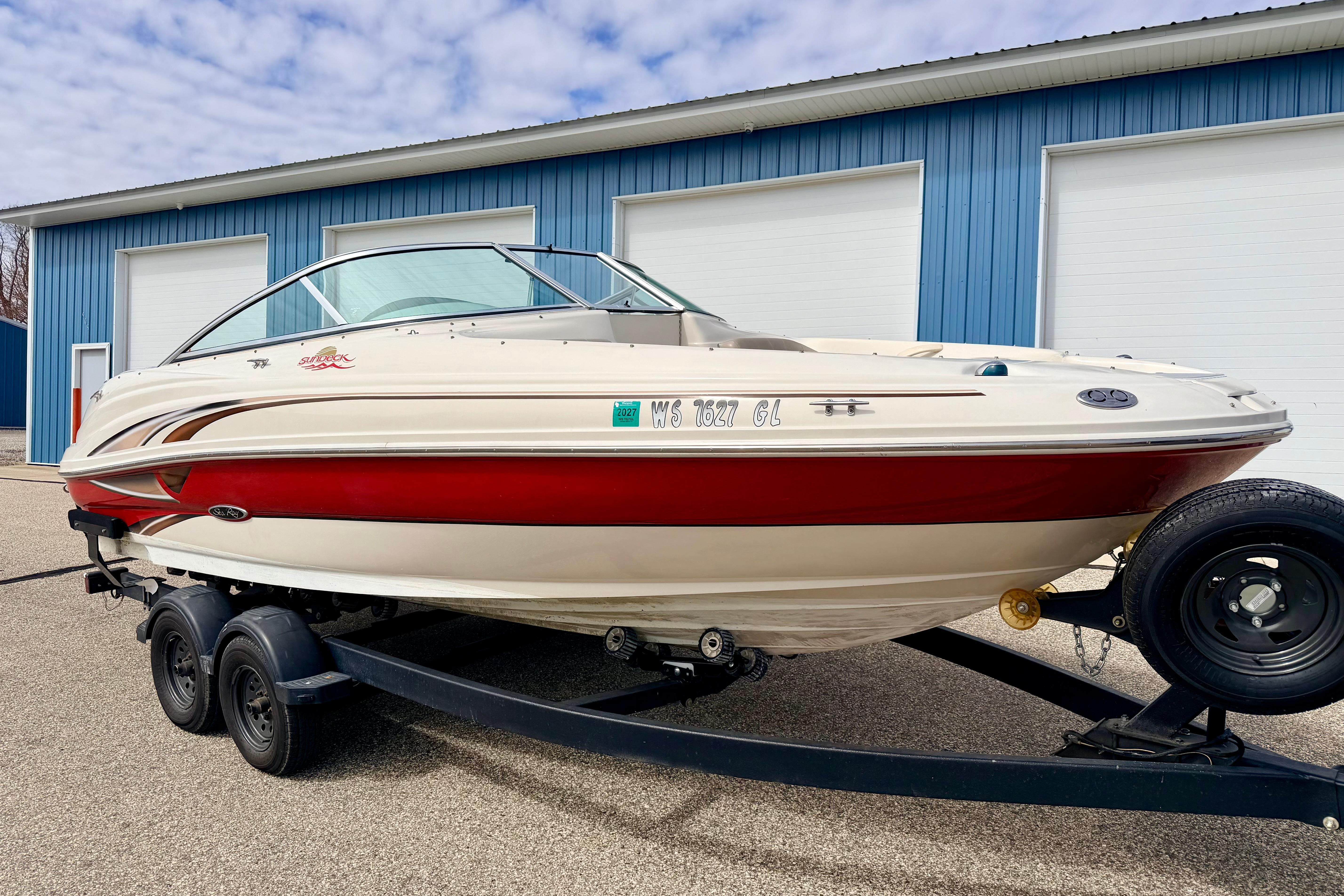 2003 Sea Ray 200 Sundeck boat on trailer, parked near blue building.