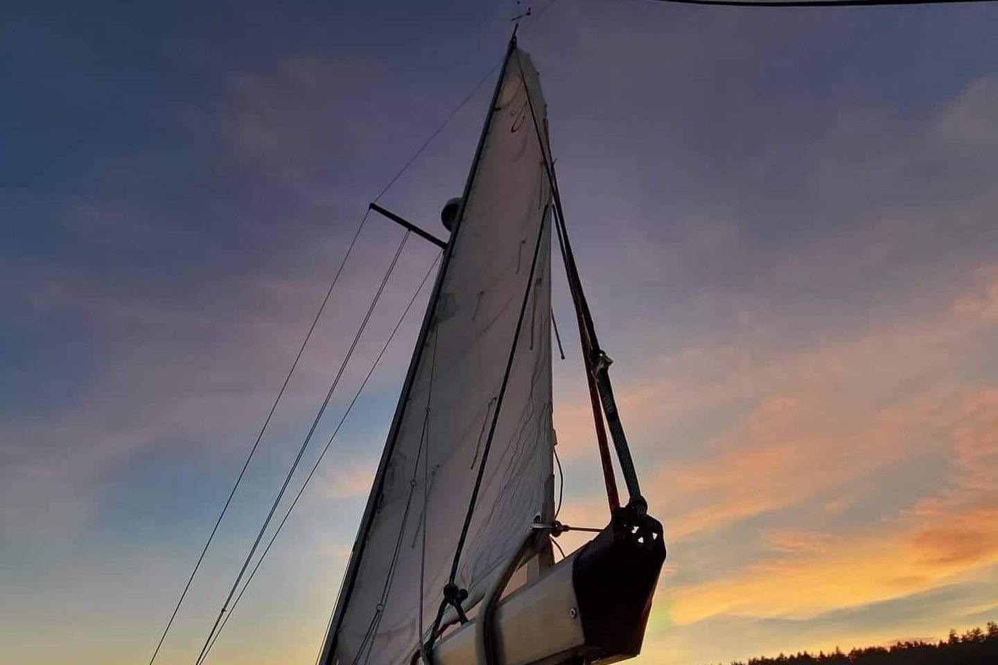 A sailboat with its sail raised against a colorful sunset.