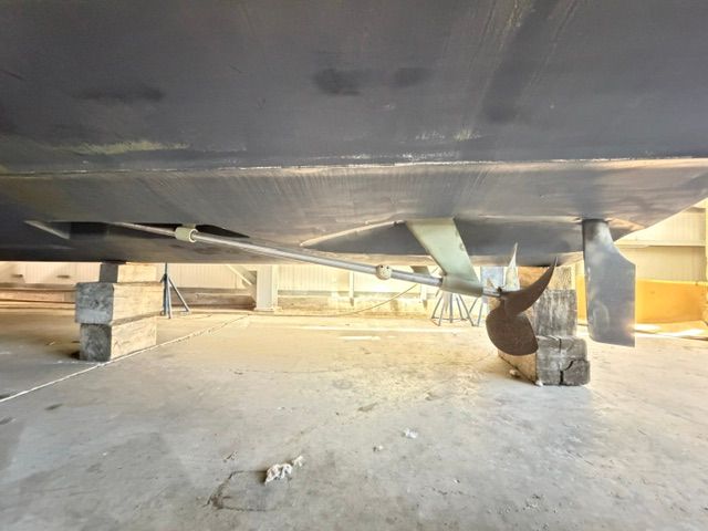 Underside of a yacht with propeller and rudder, propped up in a shipyard.