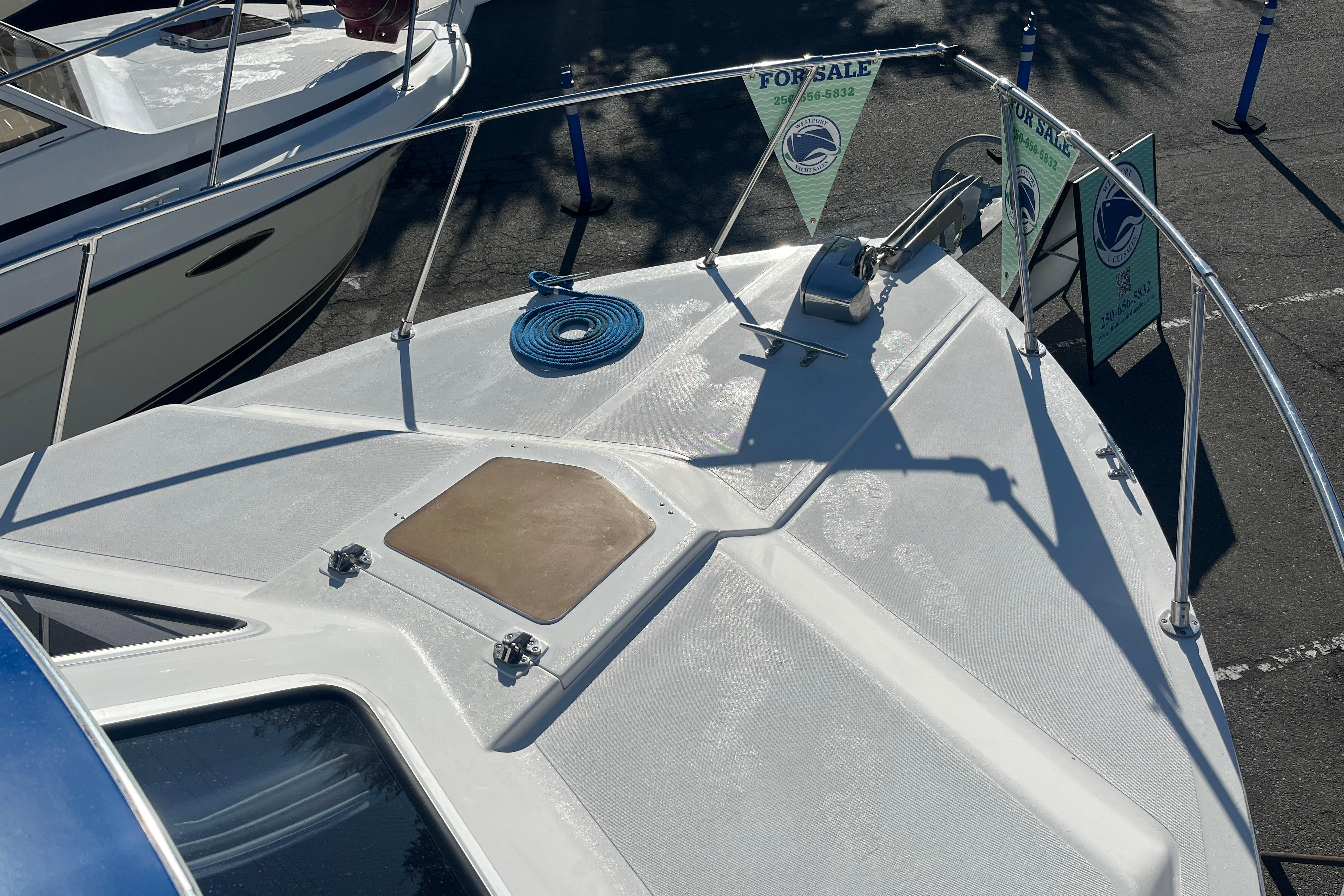 Boat deck with railing, blue rope, and "For Sale" signs in a parking lot.