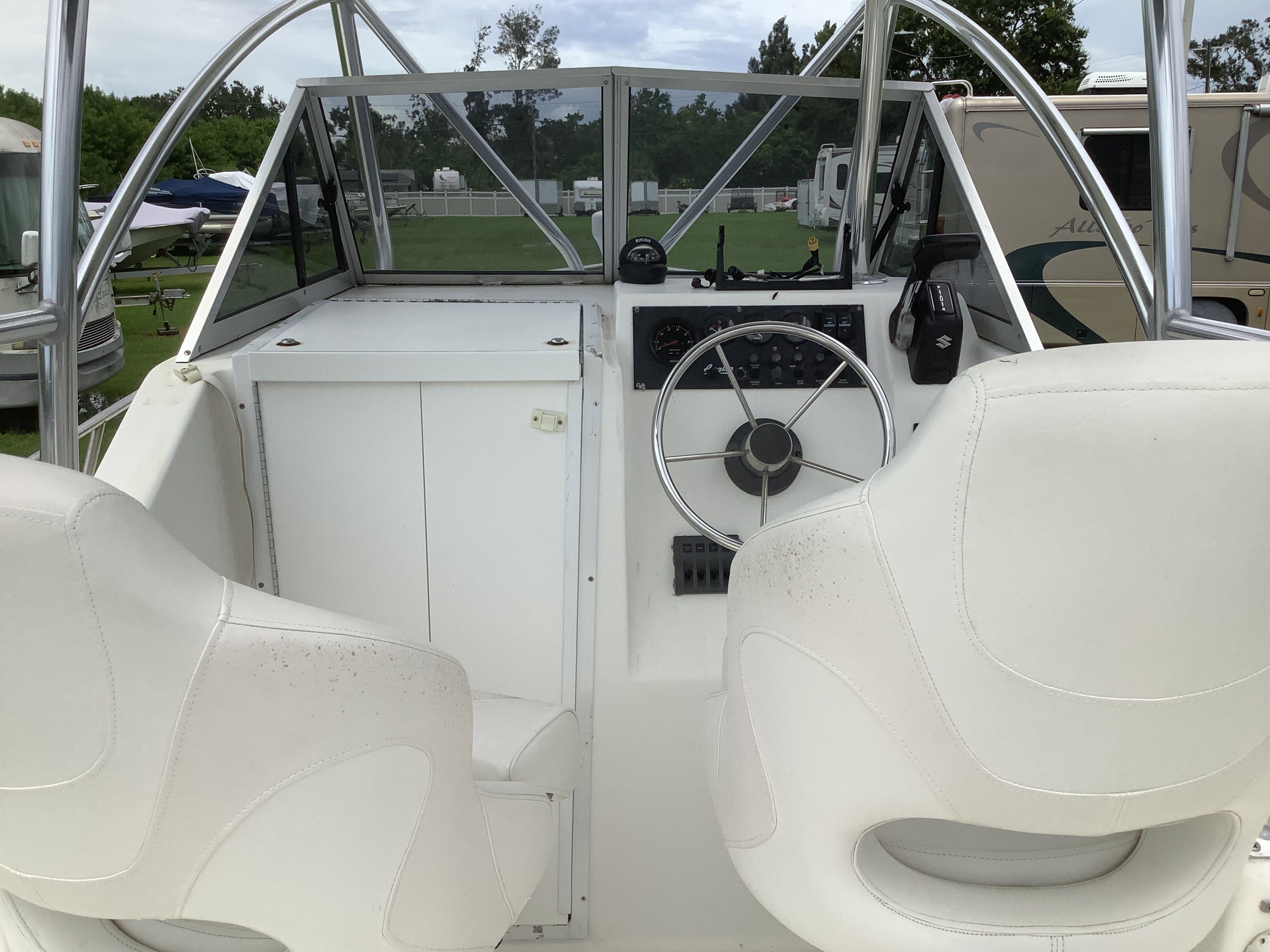 Interior view of a boat with two white seats and a steering wheel.